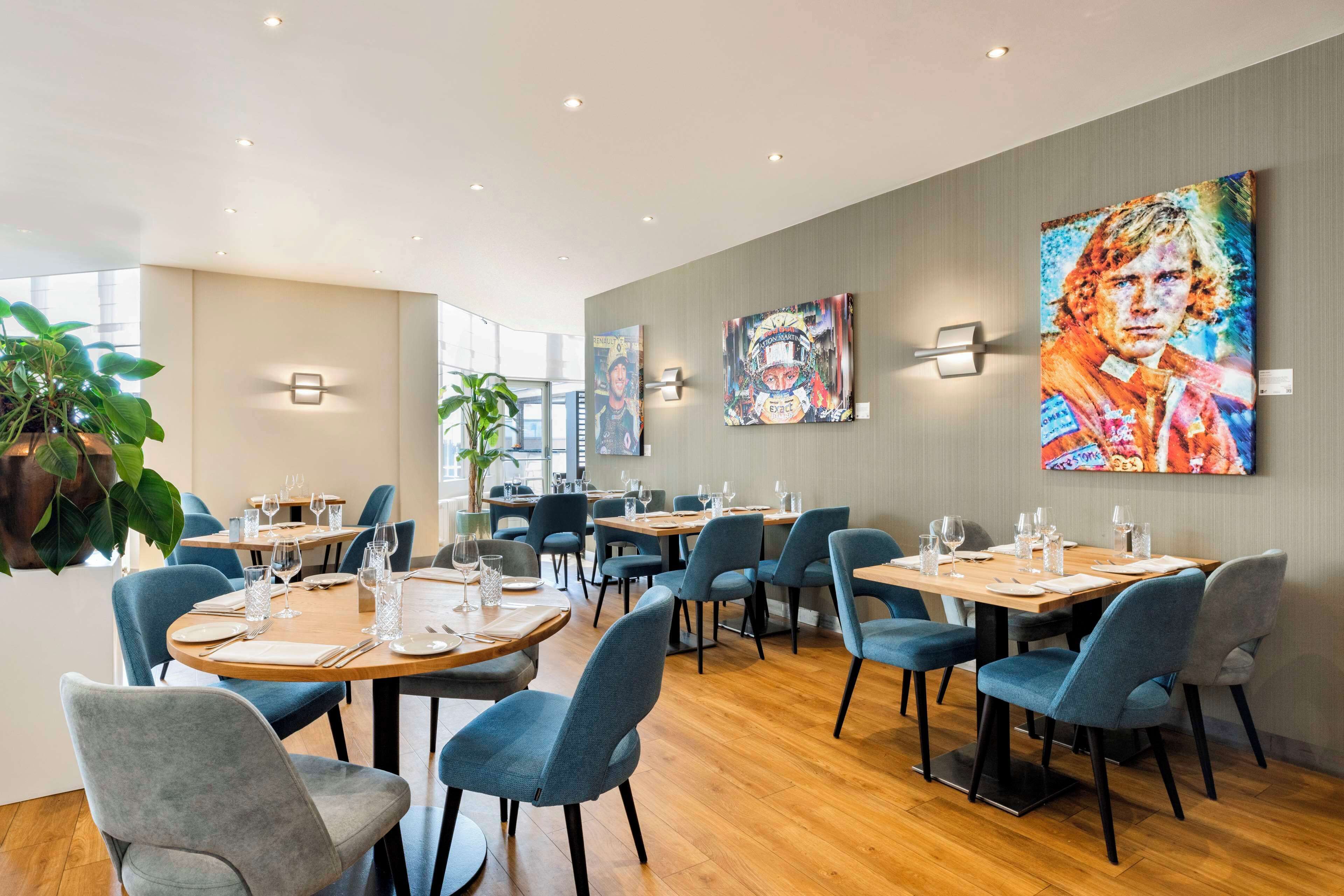 A modern restaurant with round tables, blue chairs, and artwork on the walls.