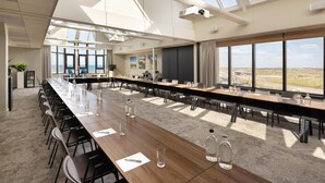 A conference room with a long table, chairs, and large windows offering a view of the landscape. - NH Zandvoort (Zandvoort)