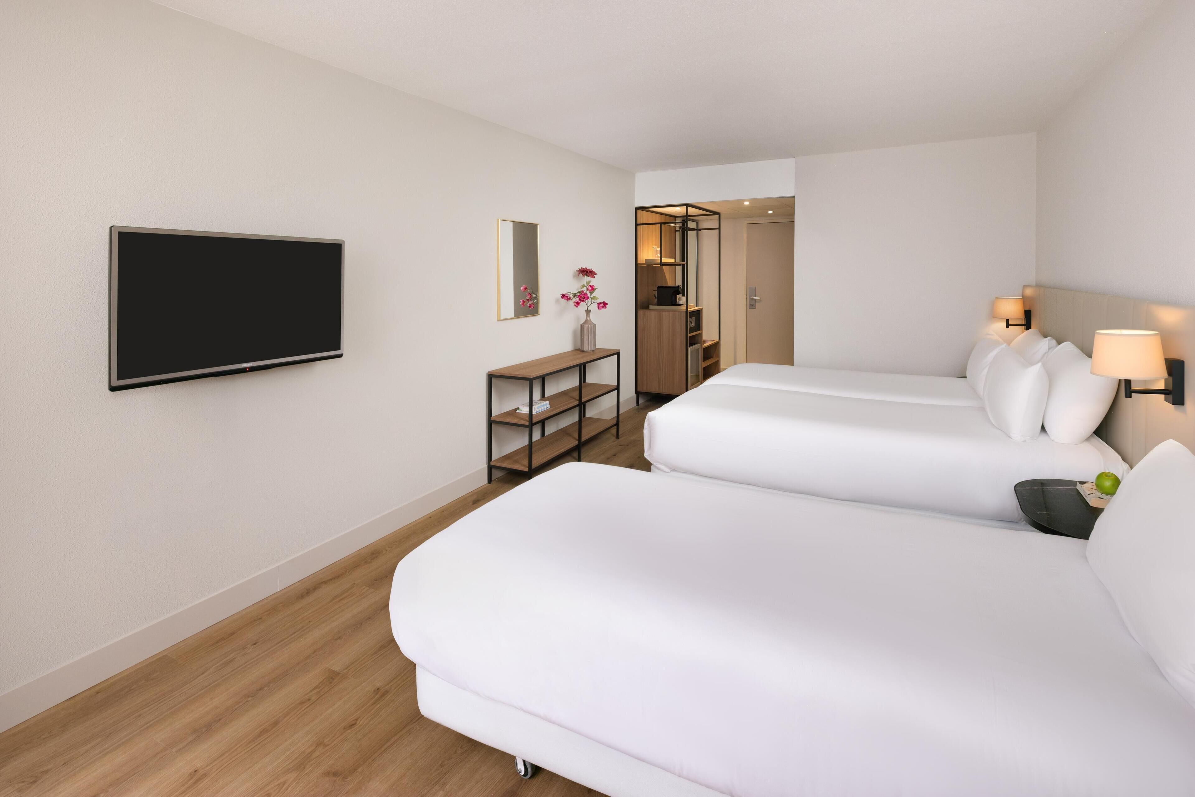 Una habitación de hotel con dos camas, televisión, una mesita y un espejo.