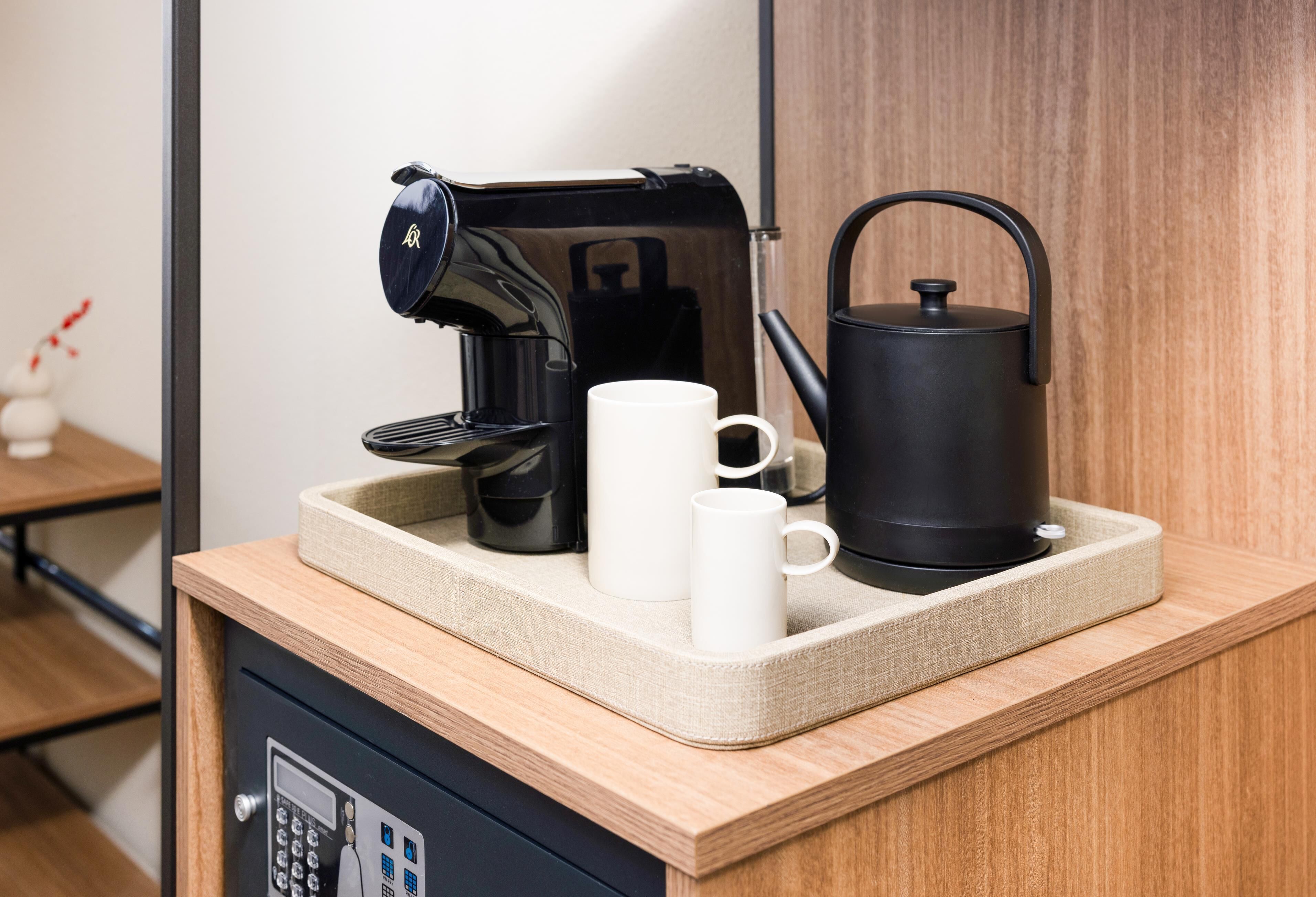 A kitchenette with a coffee maker, kettle, and two mugs on a tray.