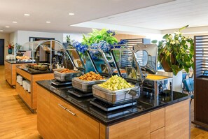 A buffet with various food options, a wooden counter, and potted plants. - NH Zandvoort (Zandvoort)