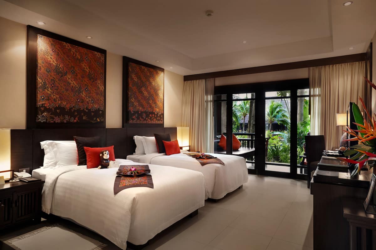 Habitación de hotel con dos camas, un escritorio y vistas al exterior.