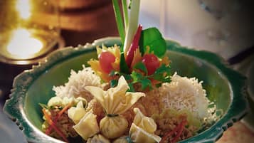 A green ceramic dish with a variety of food items, including rice, vegetables, and a decorative garnish.