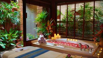 Unwind in a serene spa room with a large bathtub, two massage tables, and lush greenery.