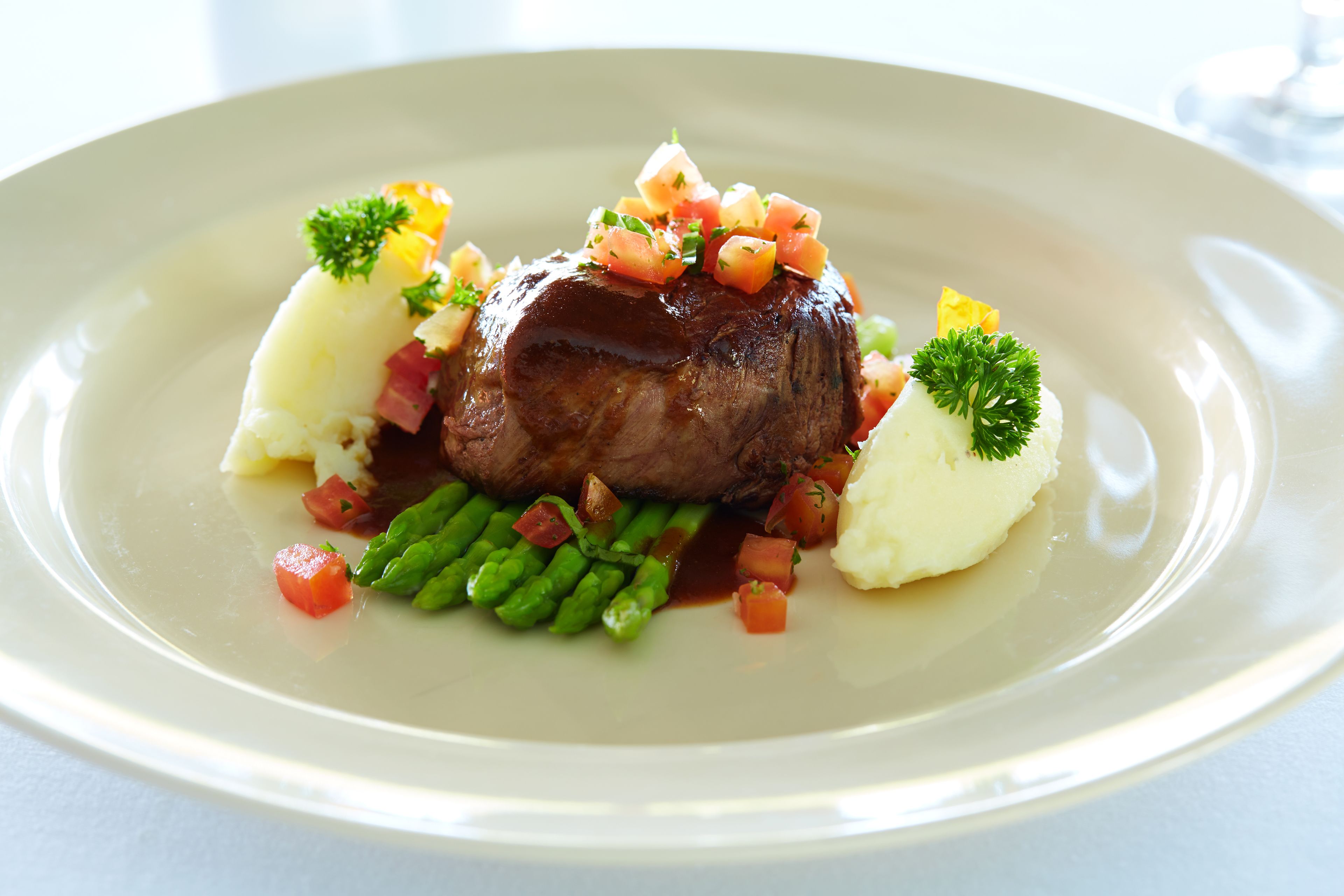 A plate of food with a piece of meat, mashed potatoes, green beans, and diced tomatoes.