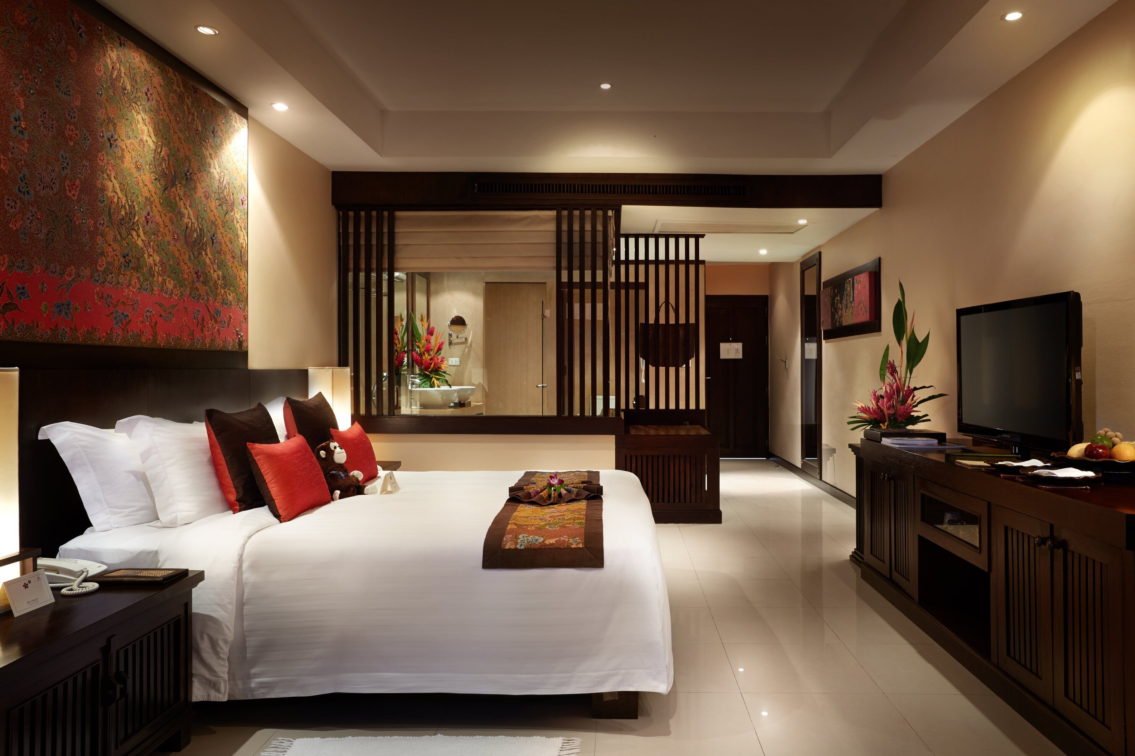 Una habitación de hotel moderna con una cama grande, una televisión, un escritorio con una computadora y un detalle decorativo en la pared.