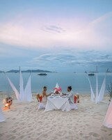 Un montaje para comer en la playa, con una mesa, sillas y un centro de mesa con velas.