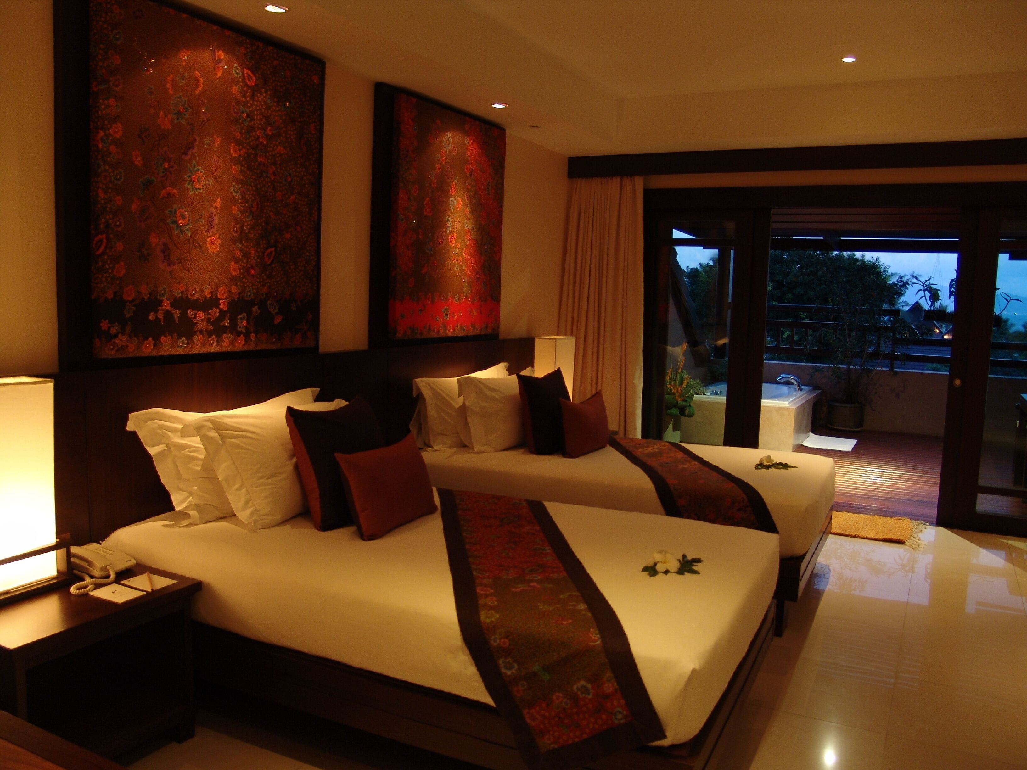 A hotel room with two beds, a nightstand with a telephone, and a large window with a view of the outdoors.