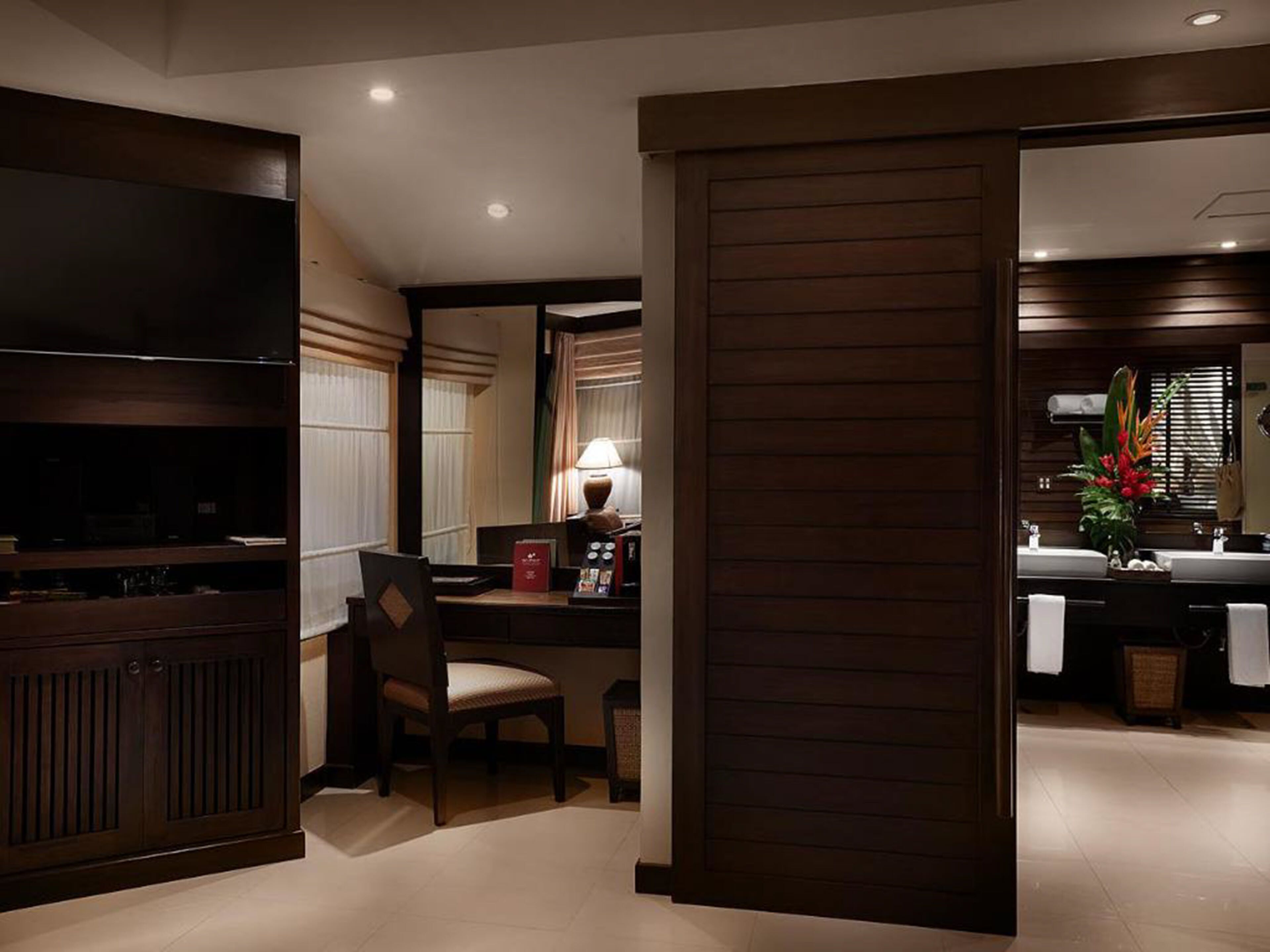 Habitació d'hotel amb televisió, escriptori amb cadira, làmpada i finestra gran amb cortines.
