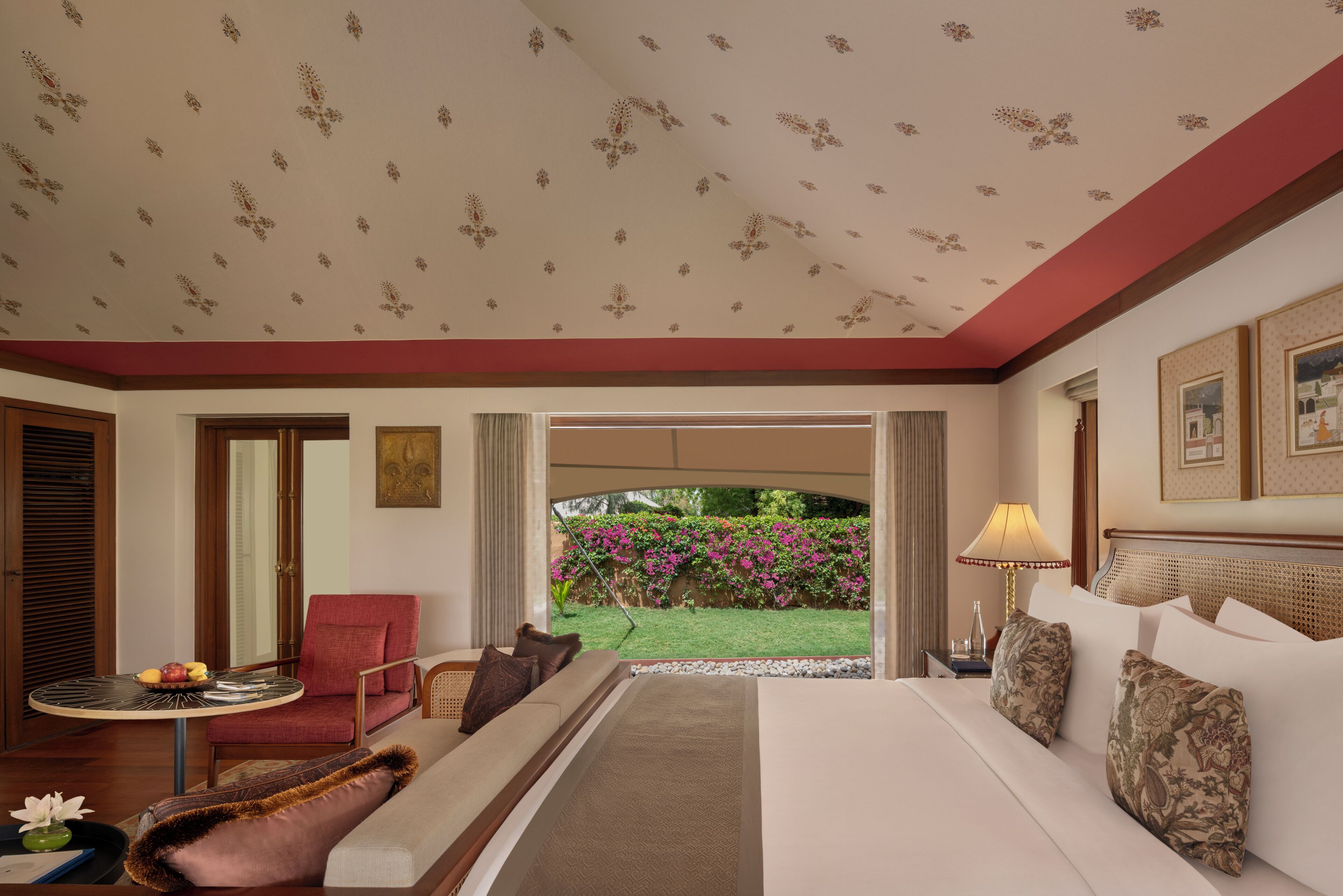 Quarto de hotel com cama, cadeira, mesa pequena e vista para um jardim.