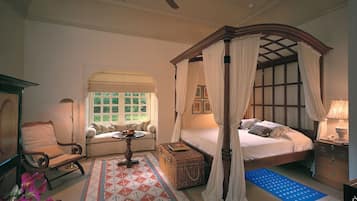 Quarto com cama de dossel, área de estar com poltrona e mesa, e janela com vista para o verde.