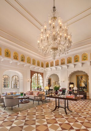 Um hall imponente com um candelabro, janelas em arco e piso padronizado.