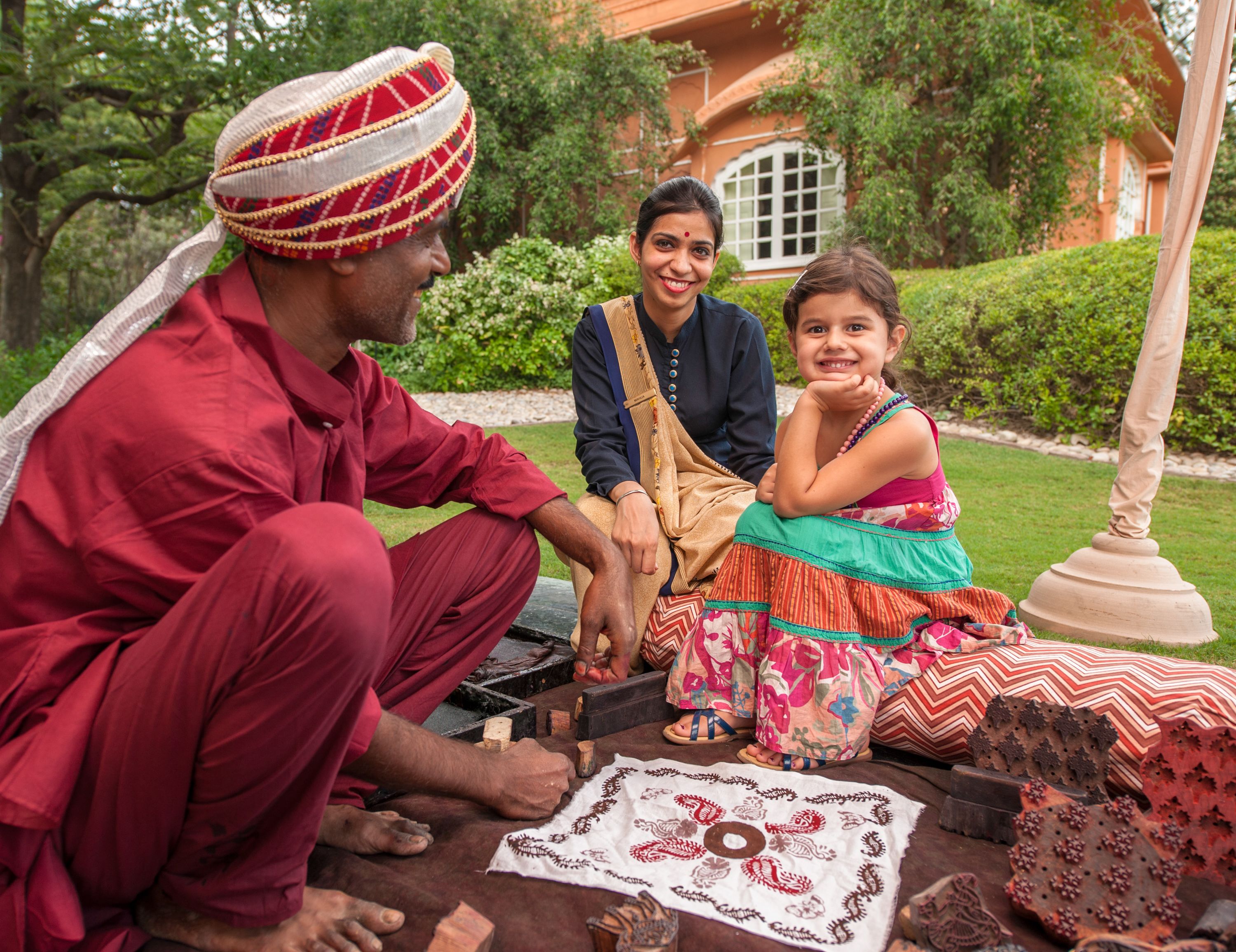 A group of people sitting outdoors, engaged in a craft activity with tools and materials on the ground.