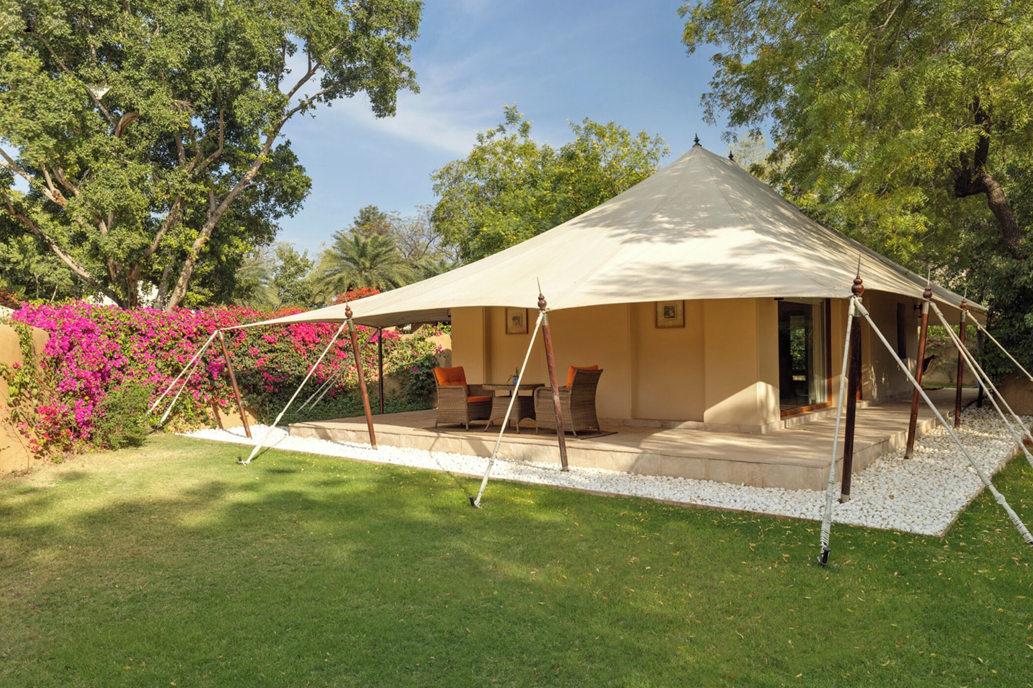 Alojamento em tenda com um alpendre, rodeado por vegeta ção e plantas floridas.