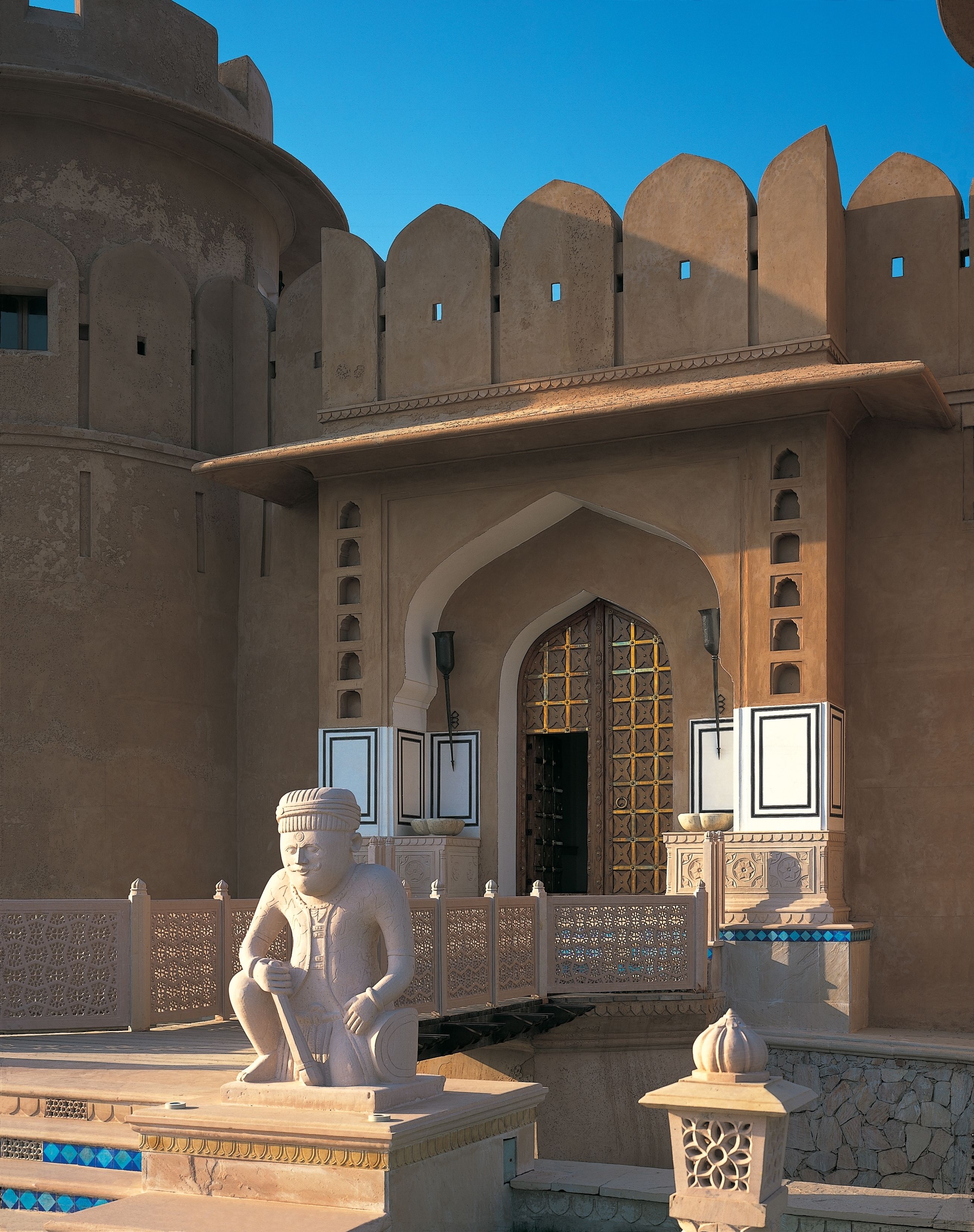 A traditional building with a large arched entrance, decorative stonework, and a statue in the foreground.