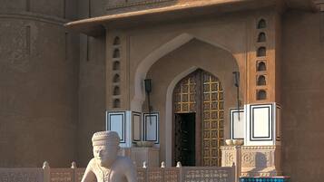 A traditional building with a large arched entrance, decorative stonework, and a statue in the foreground.