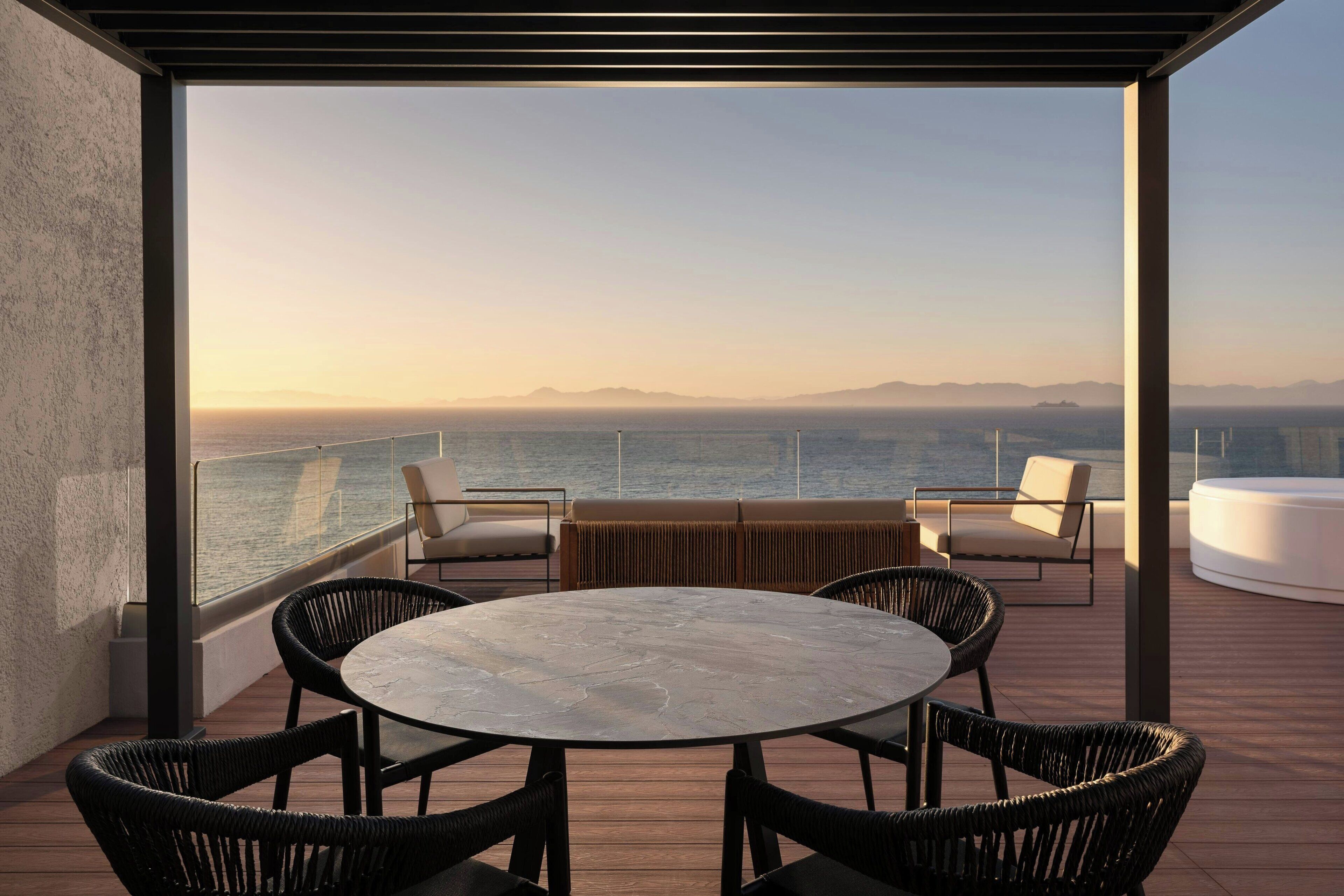 A deck with a round table and chairs, overlooking a body of water and distant mountains.