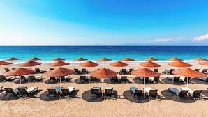 A beach with rows of sun loungers and umbrellas, a clear blue sky, and the ocean in the background.