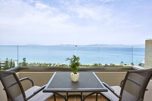 Varanda com mesa e cadeiras, um vaso de planta e vista para o mar e montanhas ao longe.
