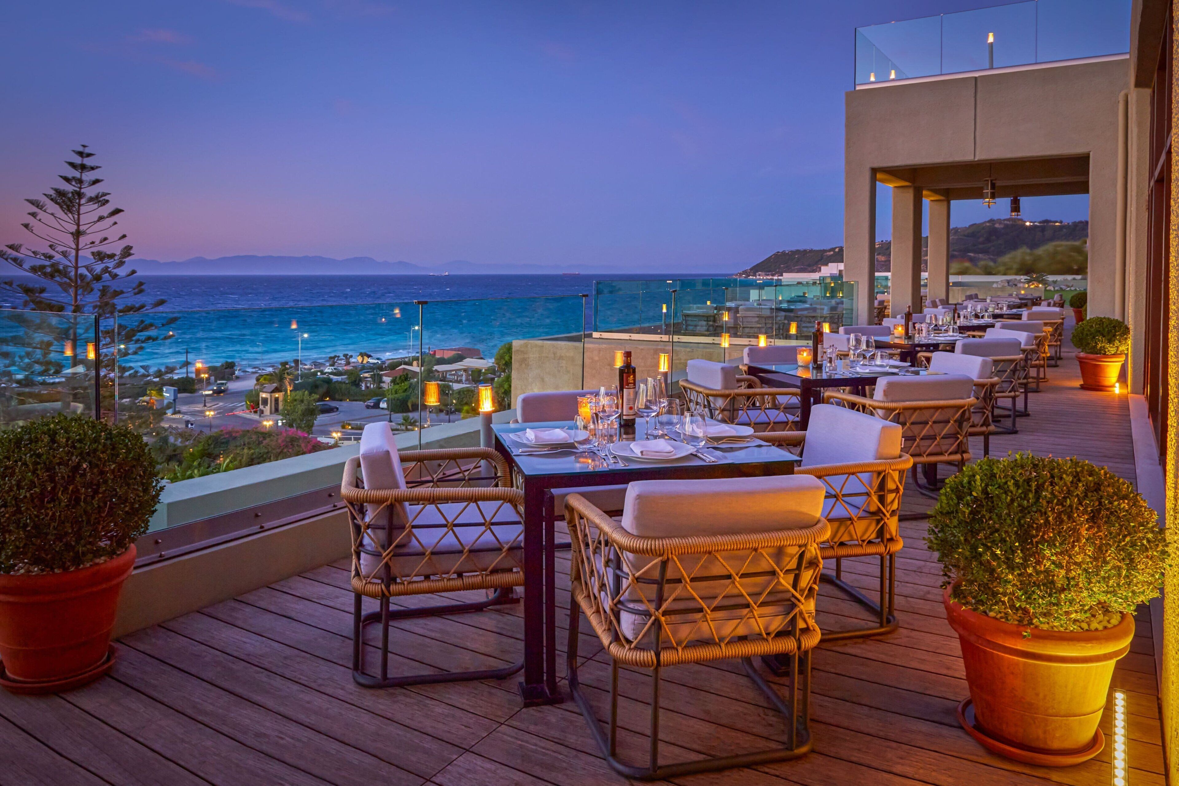 Un área de comedor al aire libre con mesas y sillas, con vistas a la costa.