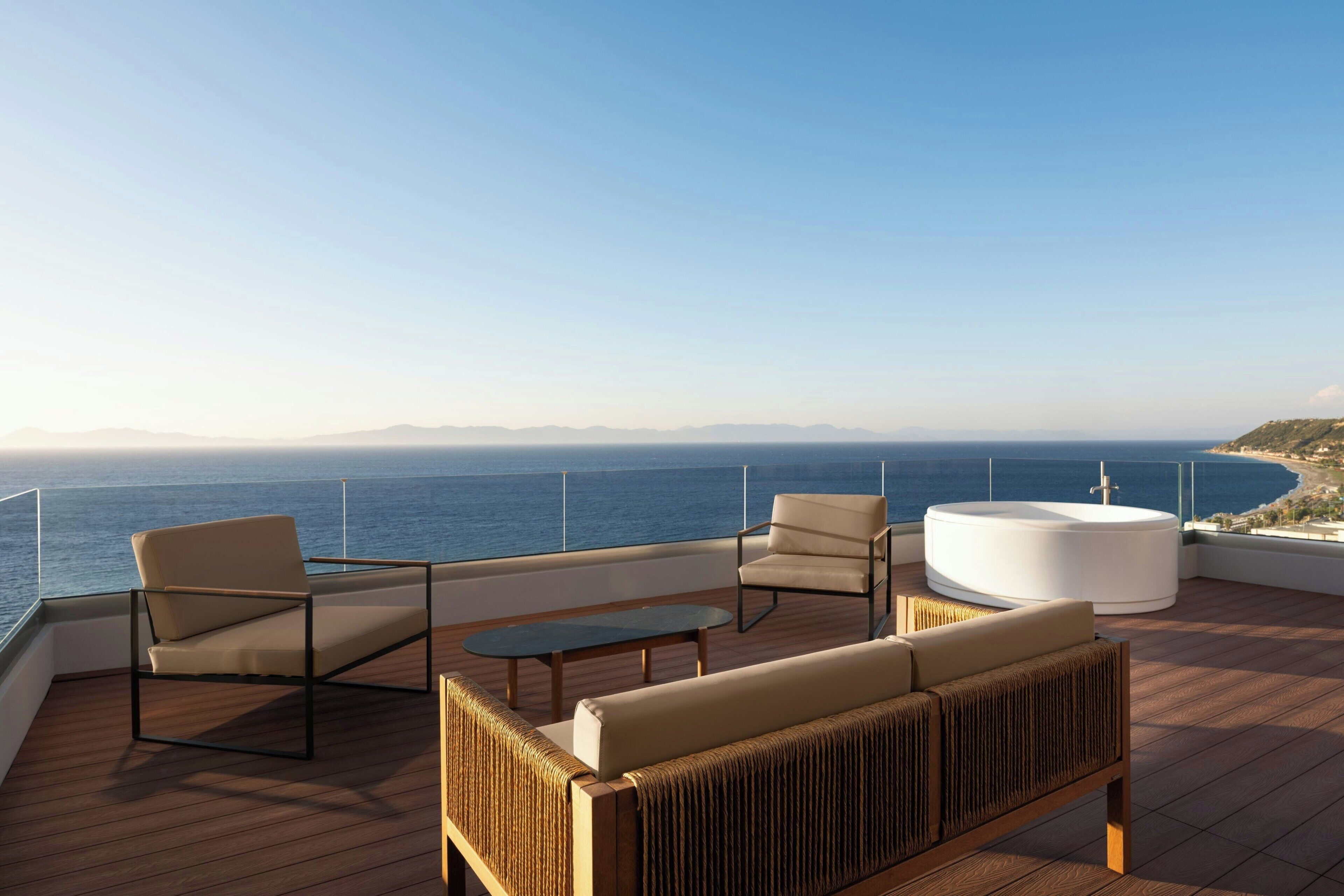 Une terrasse dotée d’un canapé, de chaises et d’une table, offrant une vue sur une étendue d’eau et sur la terre ferme au loin.