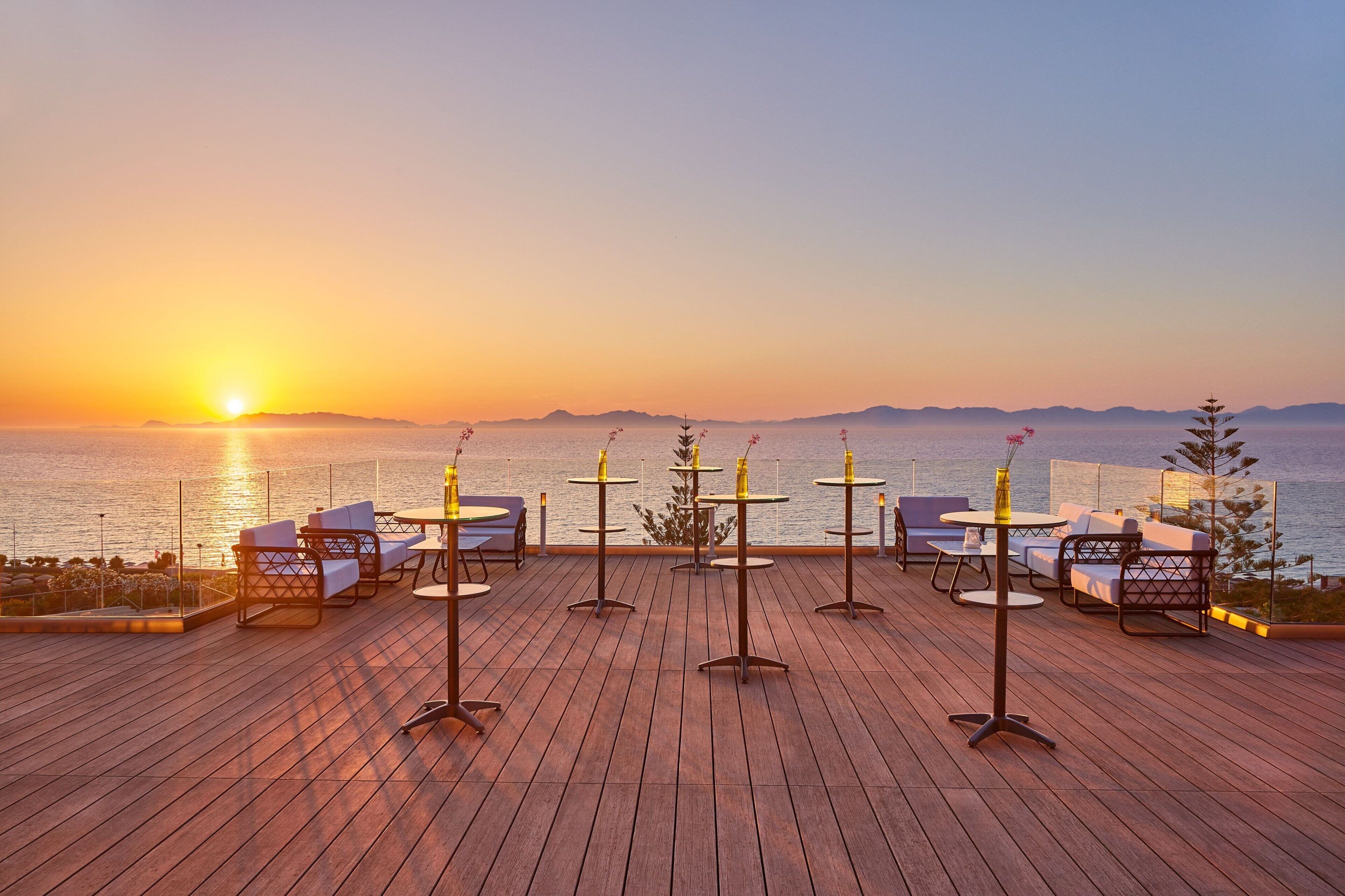 A wooden deck with outdoor seating and a view of the sunset over the water.