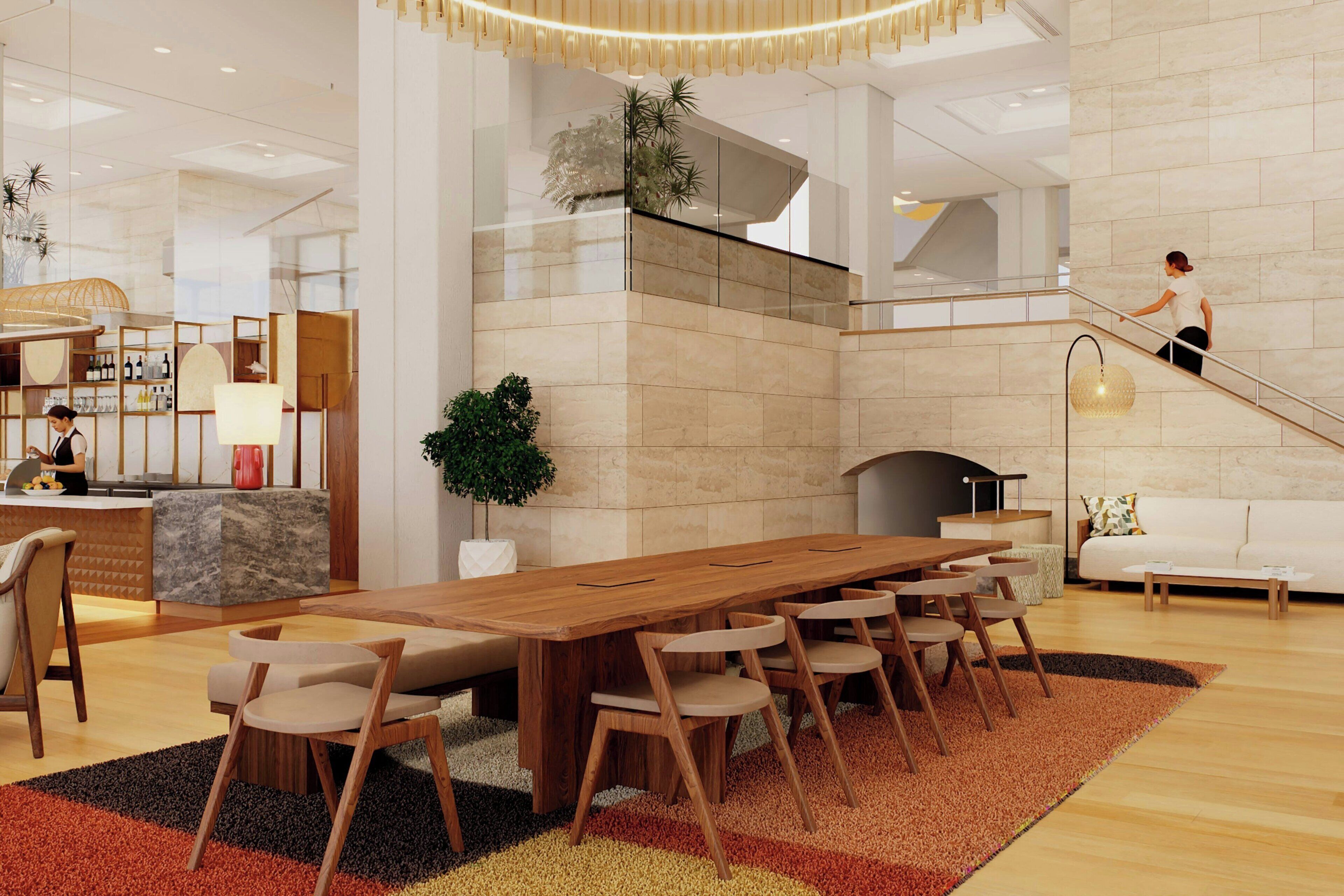 Eine moderne Hotelhalle mit einem Holztisch, Stühlen, einer Rezeption, einer Treppe und einer Couch.
