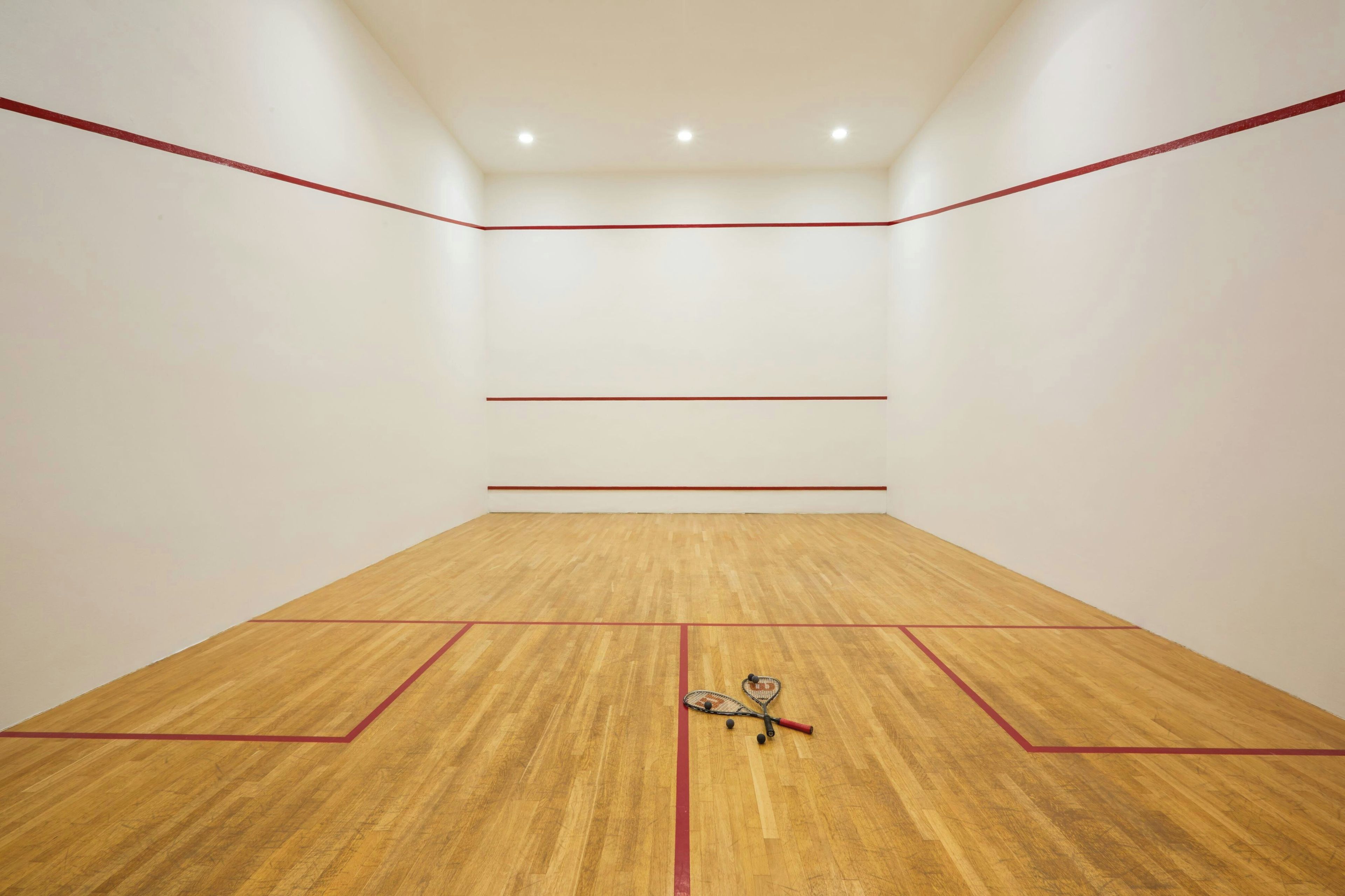 Un court de squash doté d’un plancher en bois et de lignes de démarcation rouges.