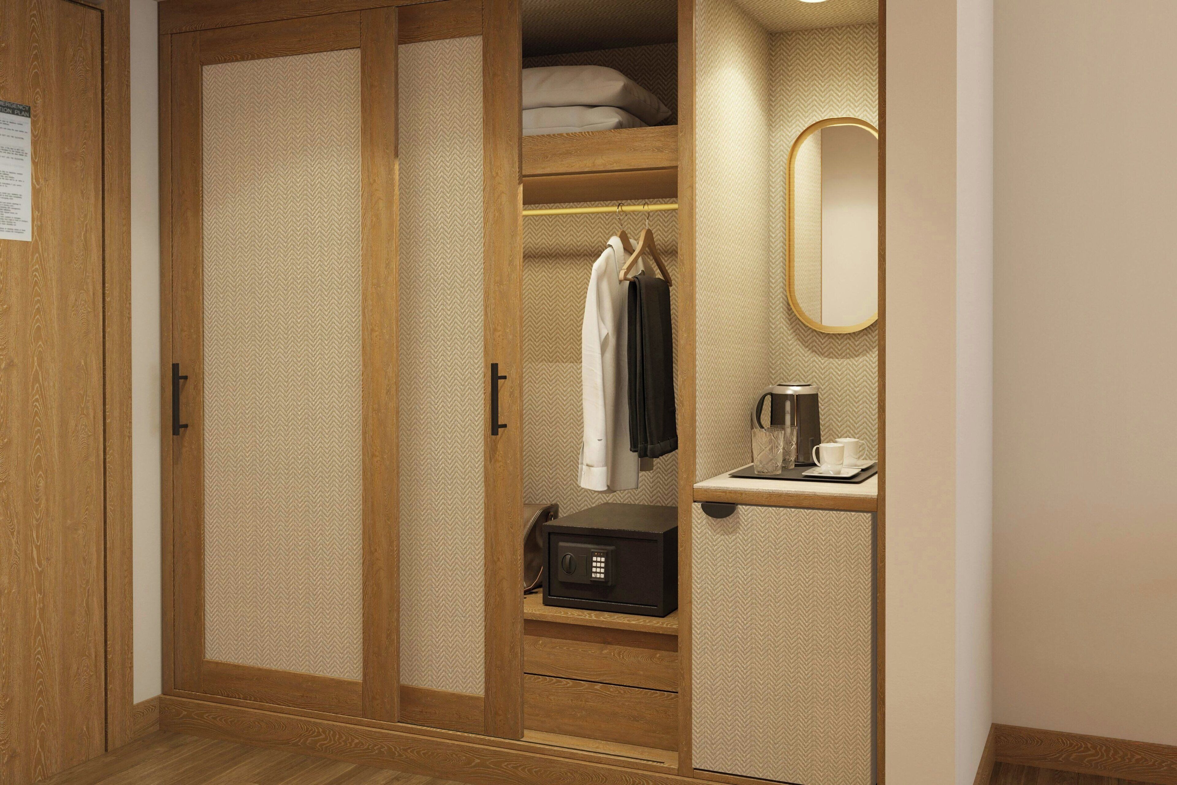 A wooden wardrobe with a mirrored door, a hanging robe, a safe, and a coffee maker.