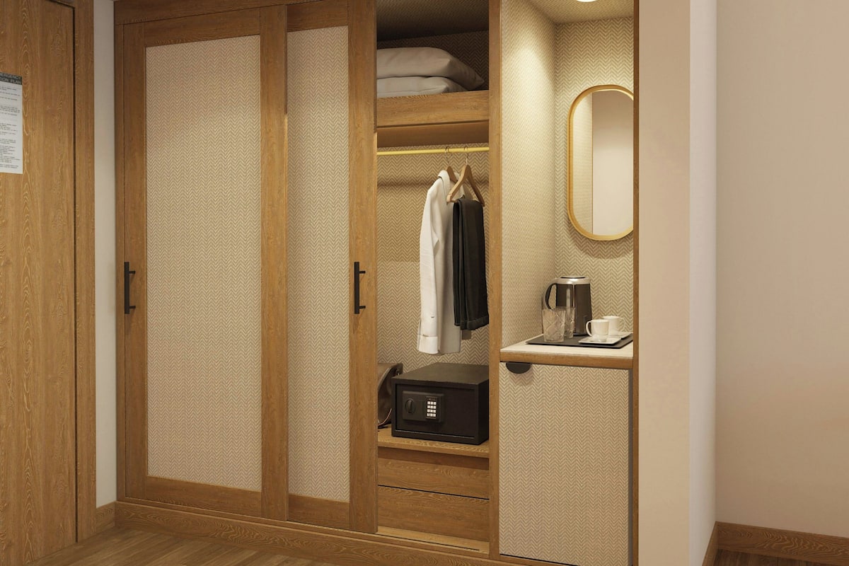 A wooden wardrobe with a mirrored door, a hanging robe, a safe, and a coffee maker.