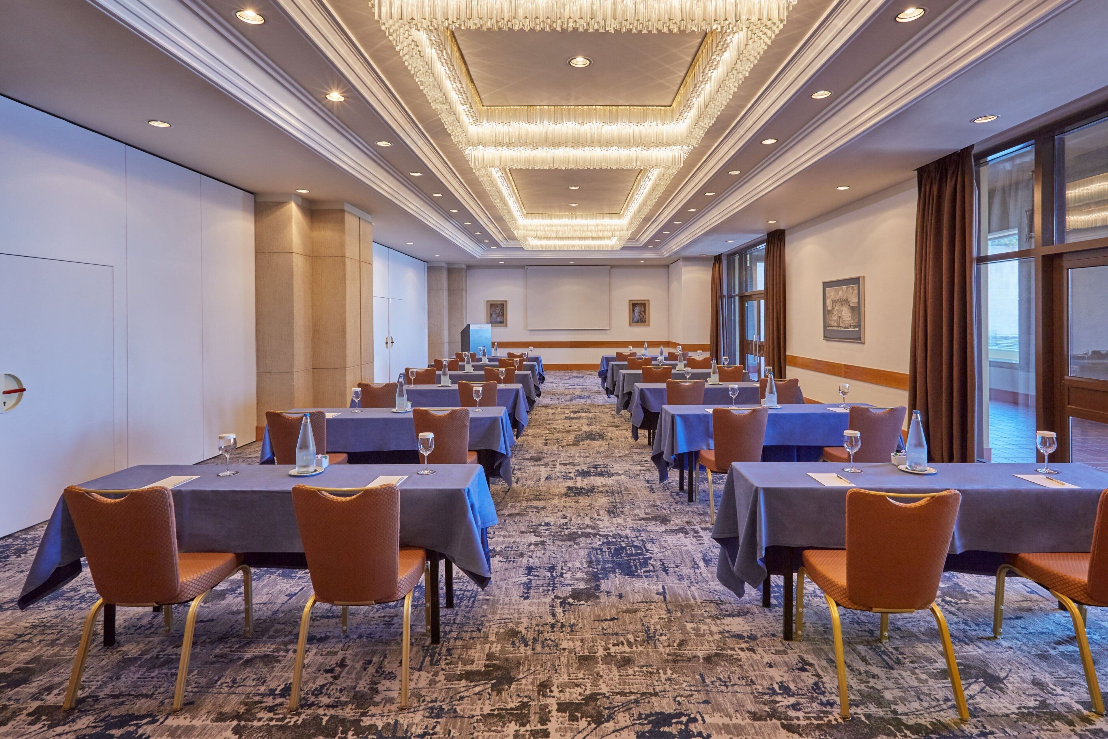 A conference room with tables and chairs, a carpeted floor, and a chandelier.