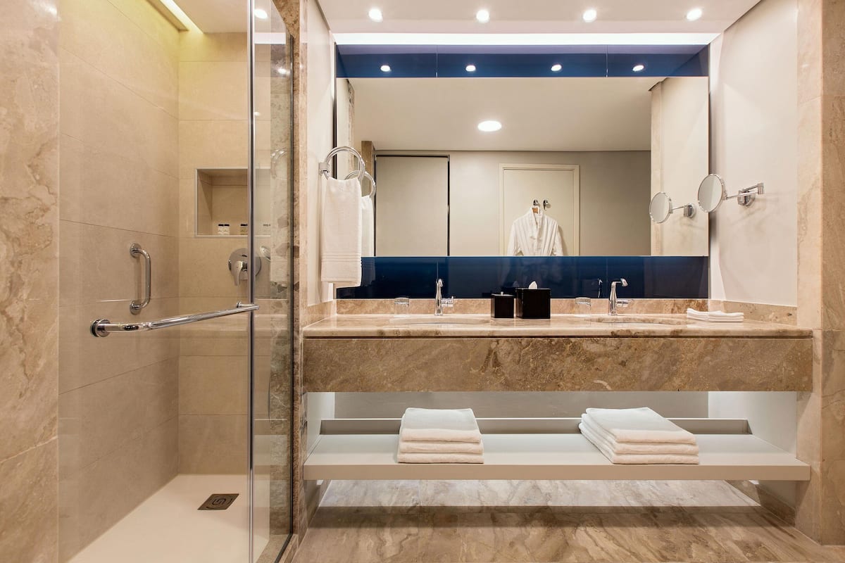 A modern bathroom with a glass shower enclosure, a vanity with a double sink, and a mirror with a robe rack.