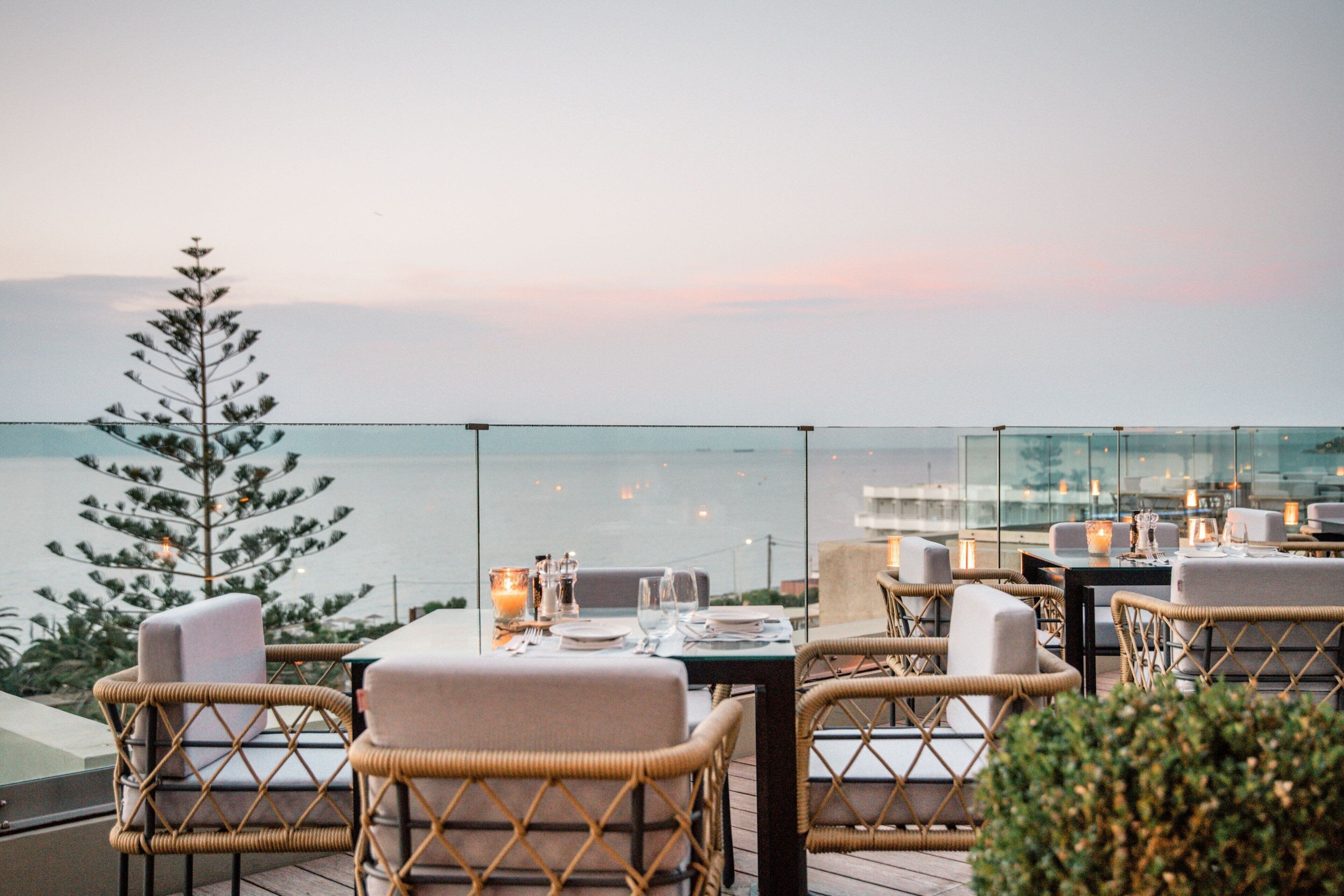 Ein Restaurant auf dem Dach mit Korbstühlen, gedeckten Tischen und Blick aufs Meer.