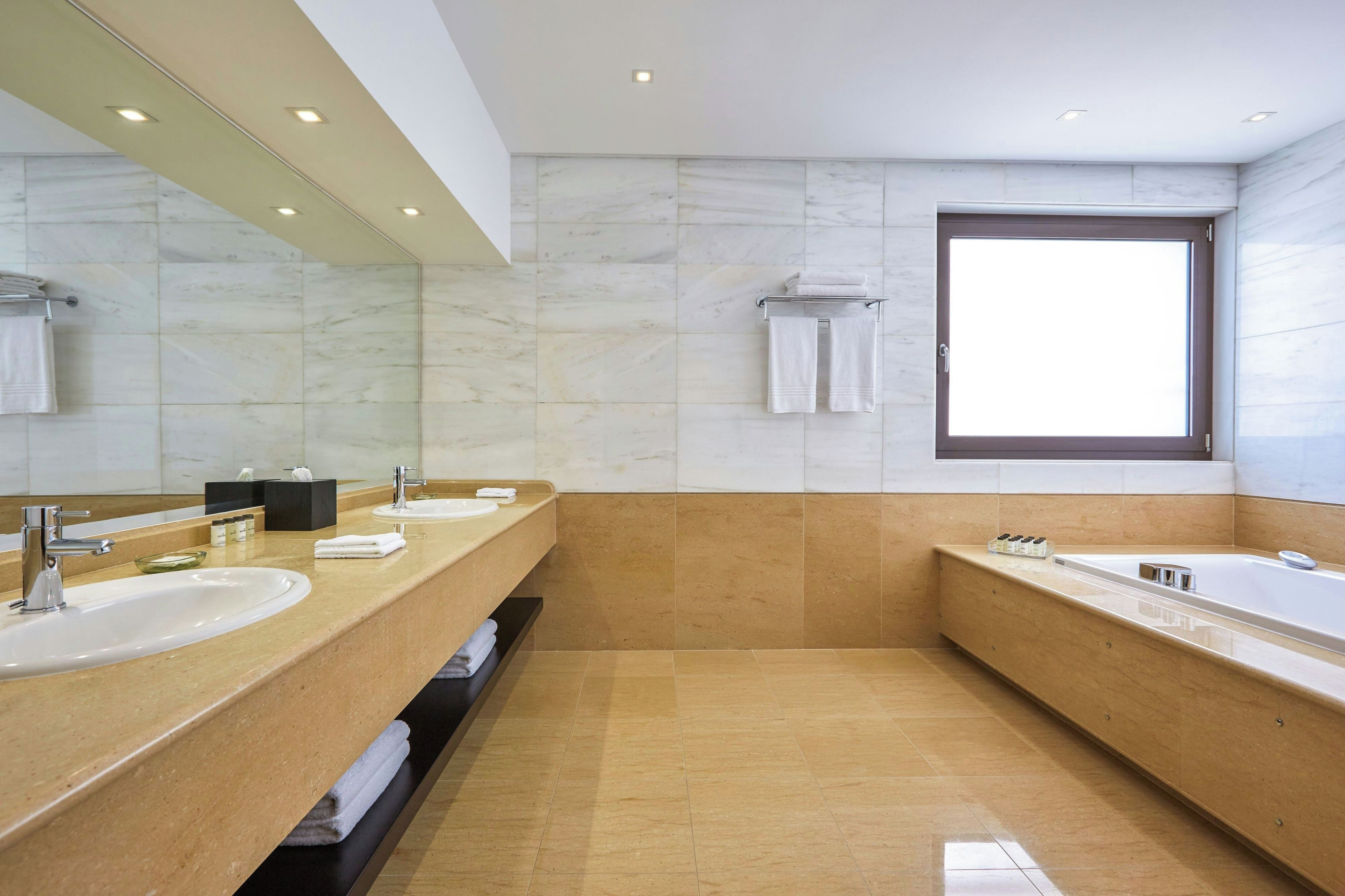Un baño moderno con dos lavamanos, un espejo grande, una bañera y una ventana.