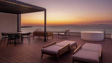 Terraza con sillones de descanso, una mesa redonda y un sofá, con vista a un cuerpo de agua al atardecer.