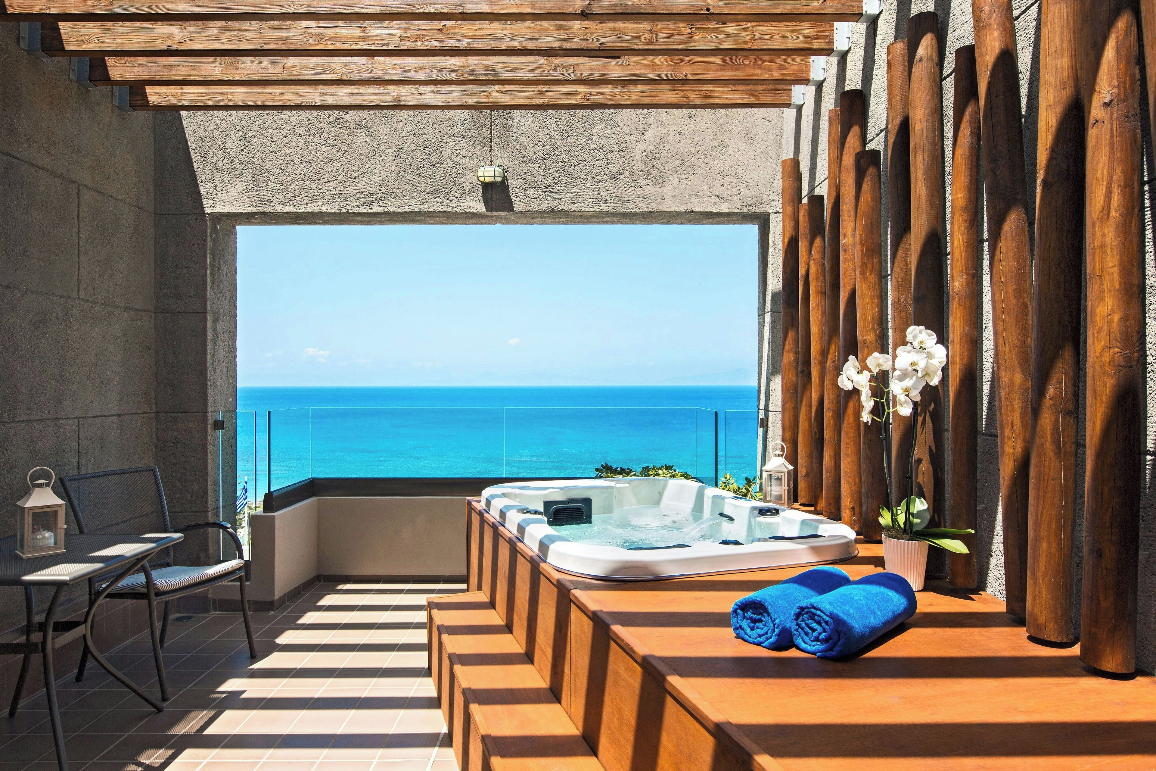 A balcony with a hot tub, seating, and a view of the ocean.