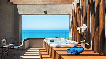 A balcony with a hot tub, seating, and a view of the ocean.