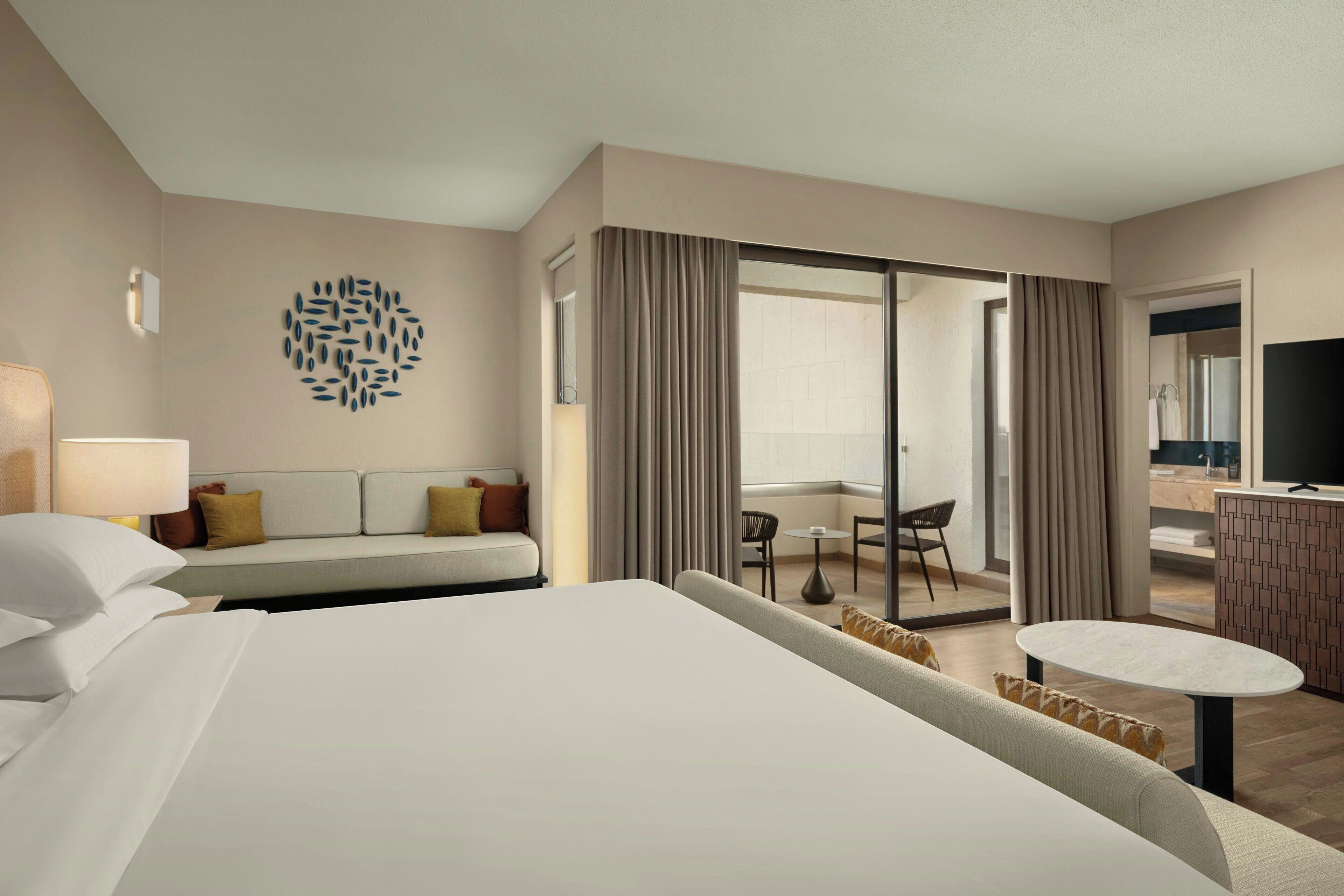Une chambre d’hôtel avec un grand lit, un canapé, une petite table, une télévision et un balcon avec vue.