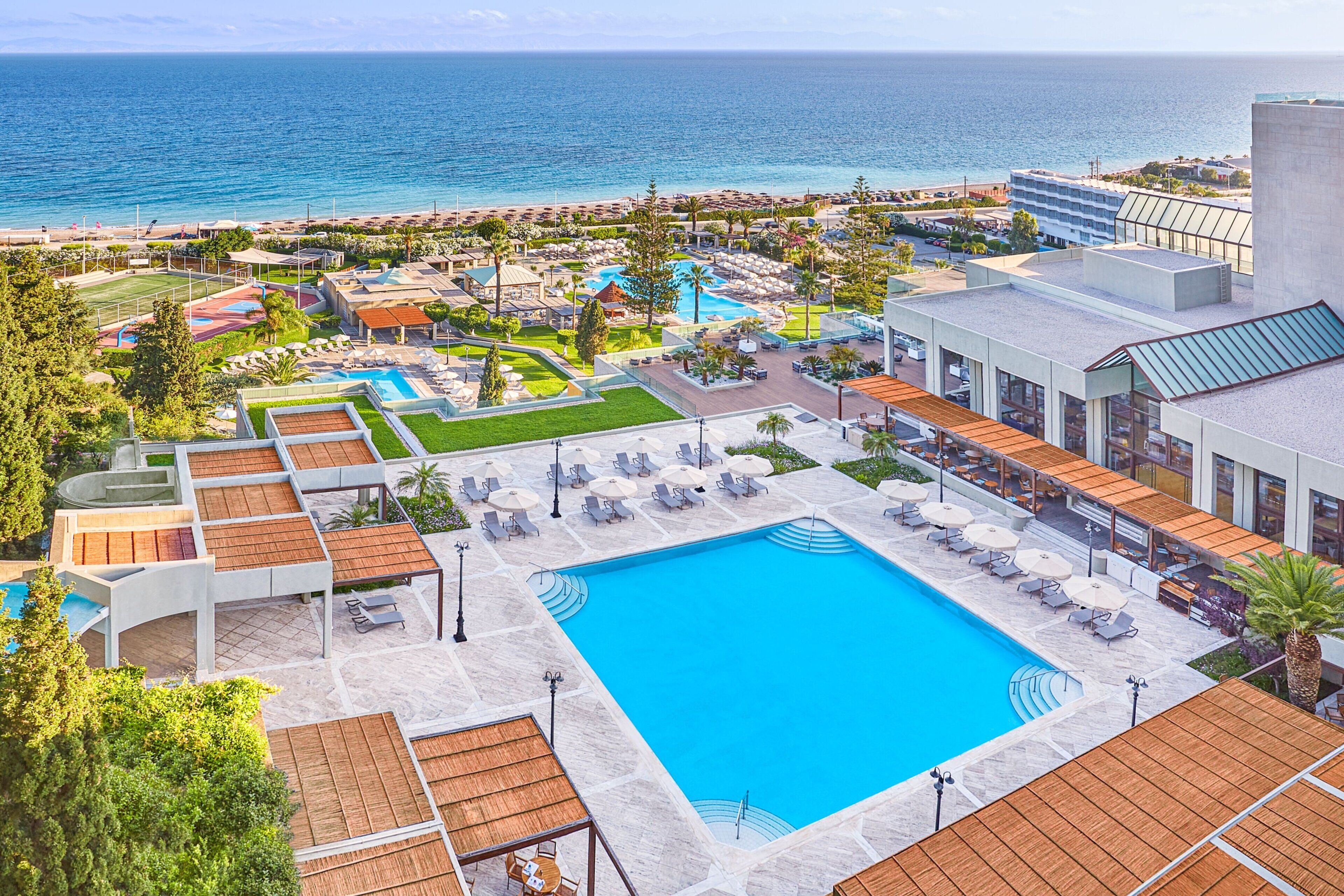 A resort with a large swimming pool, outdoor seating areas, and a view of the ocean.