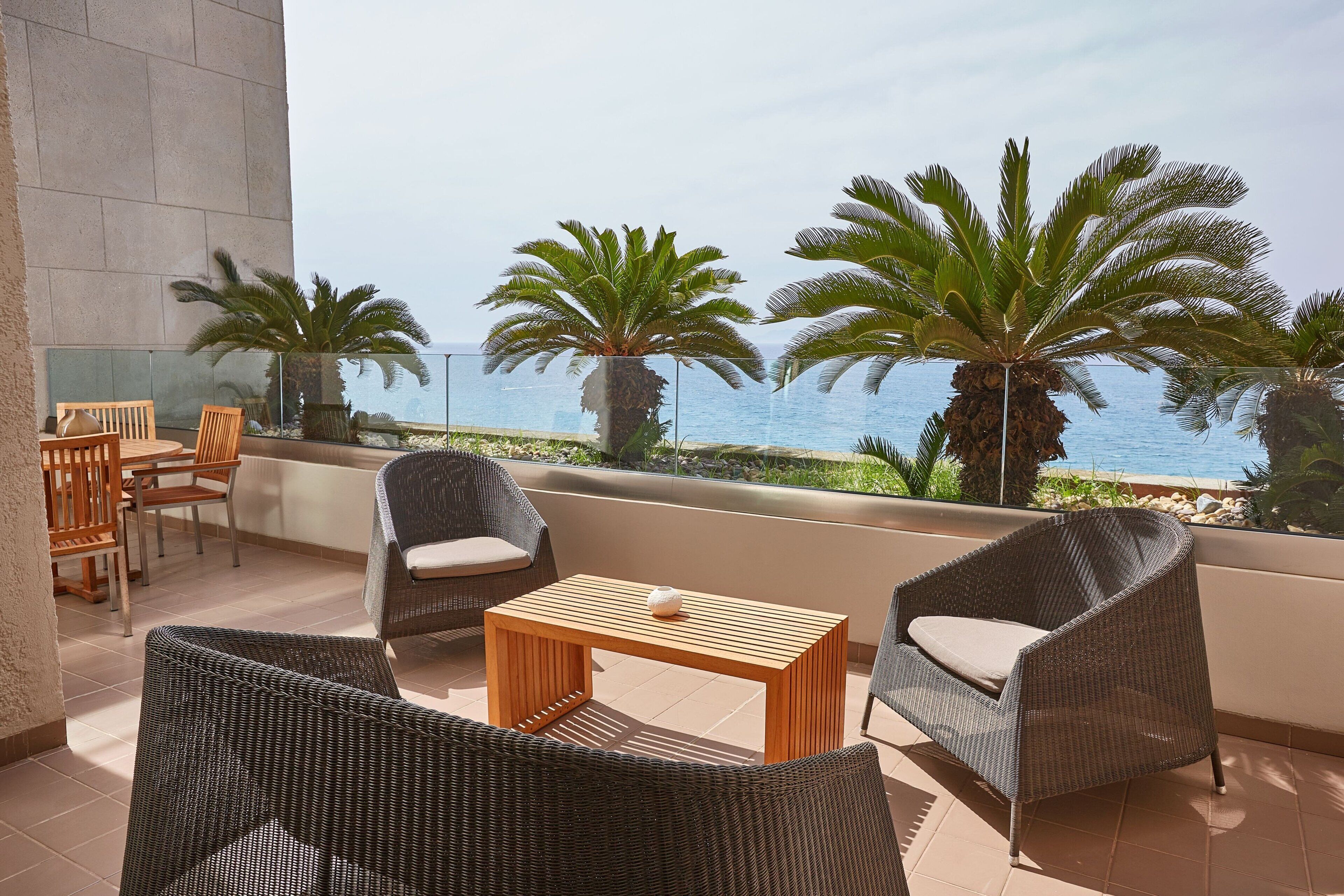 A balcony with wicker furniture, a wooden table, and palm trees.