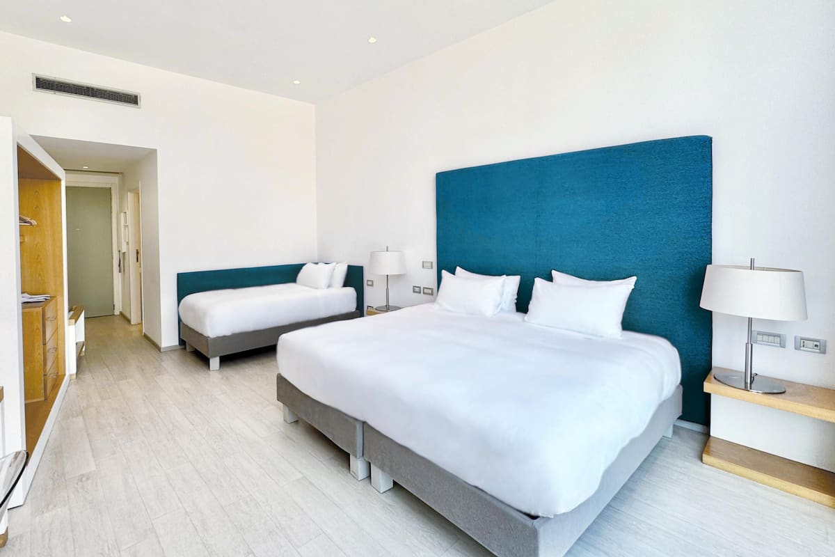 Une chambre d’hôtel moderne avec deux lits simples, un grand mur d’accent bleu et une armoire en bois.