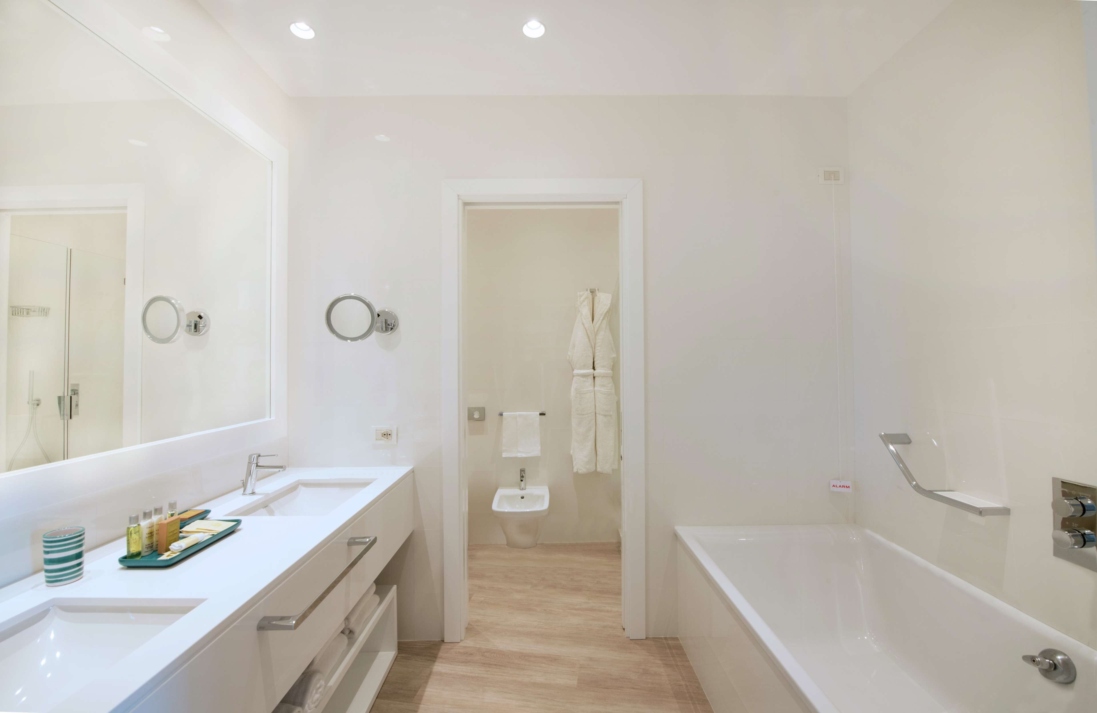A modern bathroom with a large mirror, two sinks, a bathtub, and a shower area.
