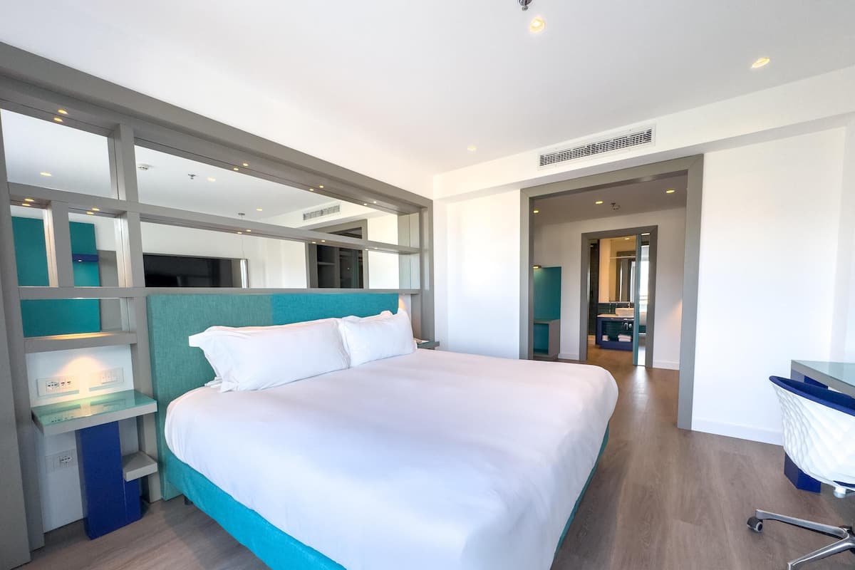 Une chambre d’hôtel moderne, dotée d’un grand lit, d’un bureau et d’une salle de bain visible à travers une porte ouverte.