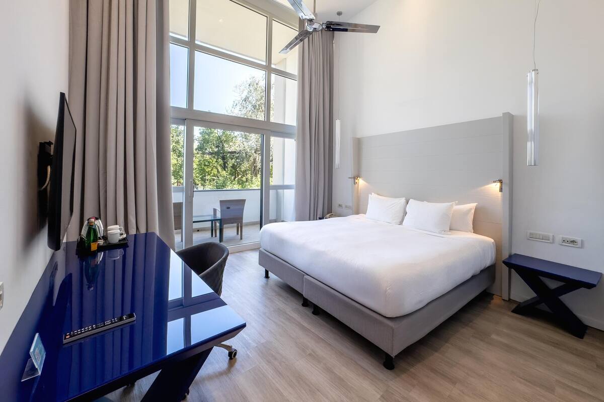 Une chambre d’hôtel moderne, dotée d’un grand lit, d’un bureau, d’une chaise et offrant une vue sur l’extérieur.