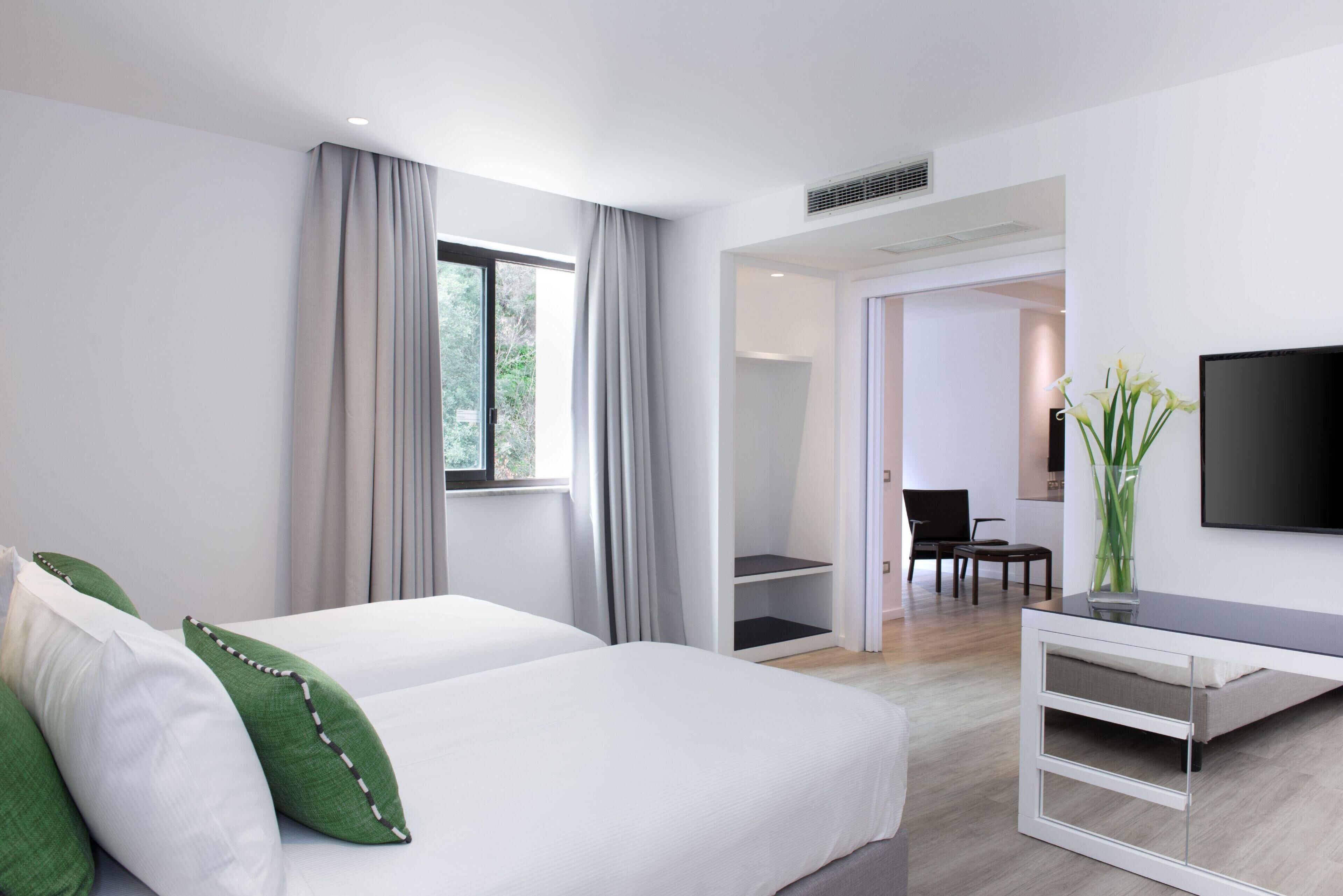 A modern hotel room with a bed, a desk, a chair, a TV, and a view of the outdoors.