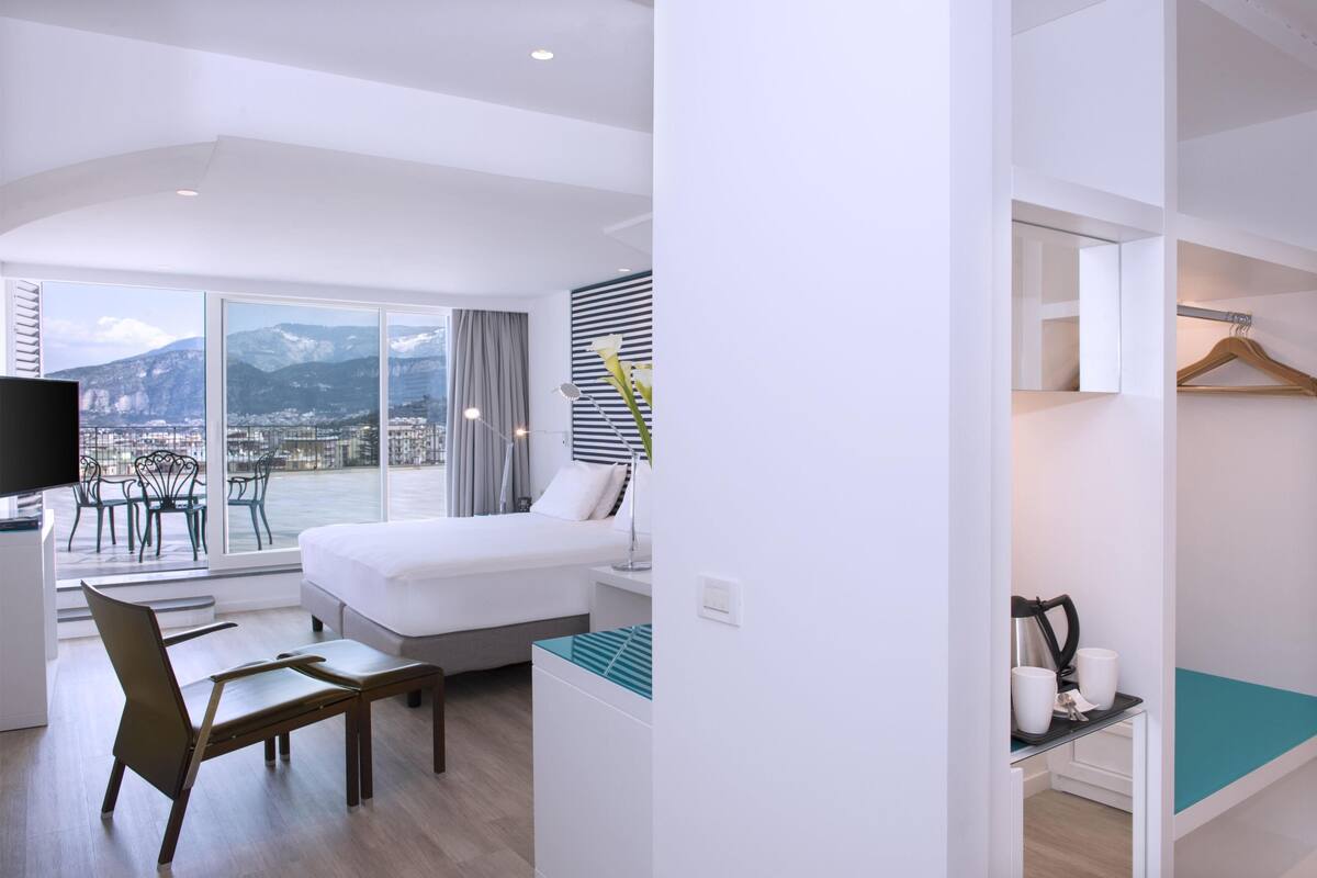 Une chambre d’hôtel équipée d’un lit, d’un bureau, d’une chaise, d’une télévision et offrant une vue sur les montagnes.