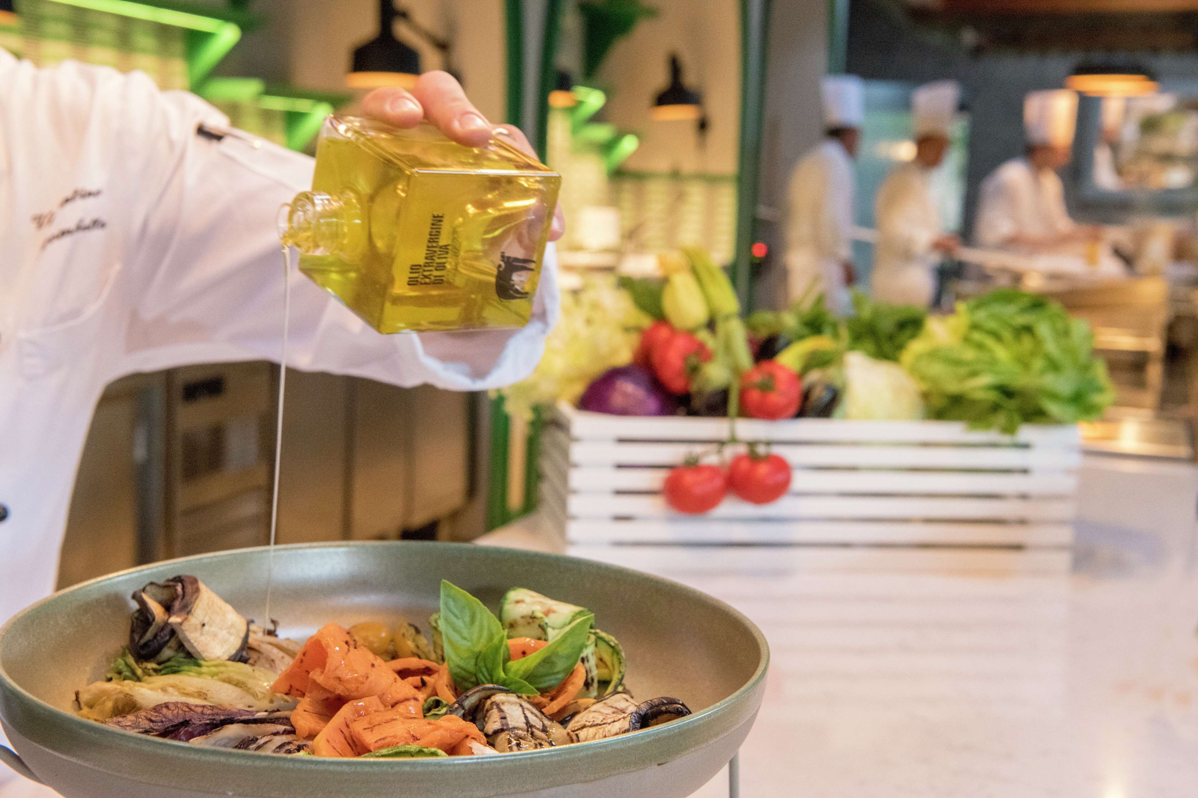 Un chef vierte aceite sobre una ensalada en un tazón.