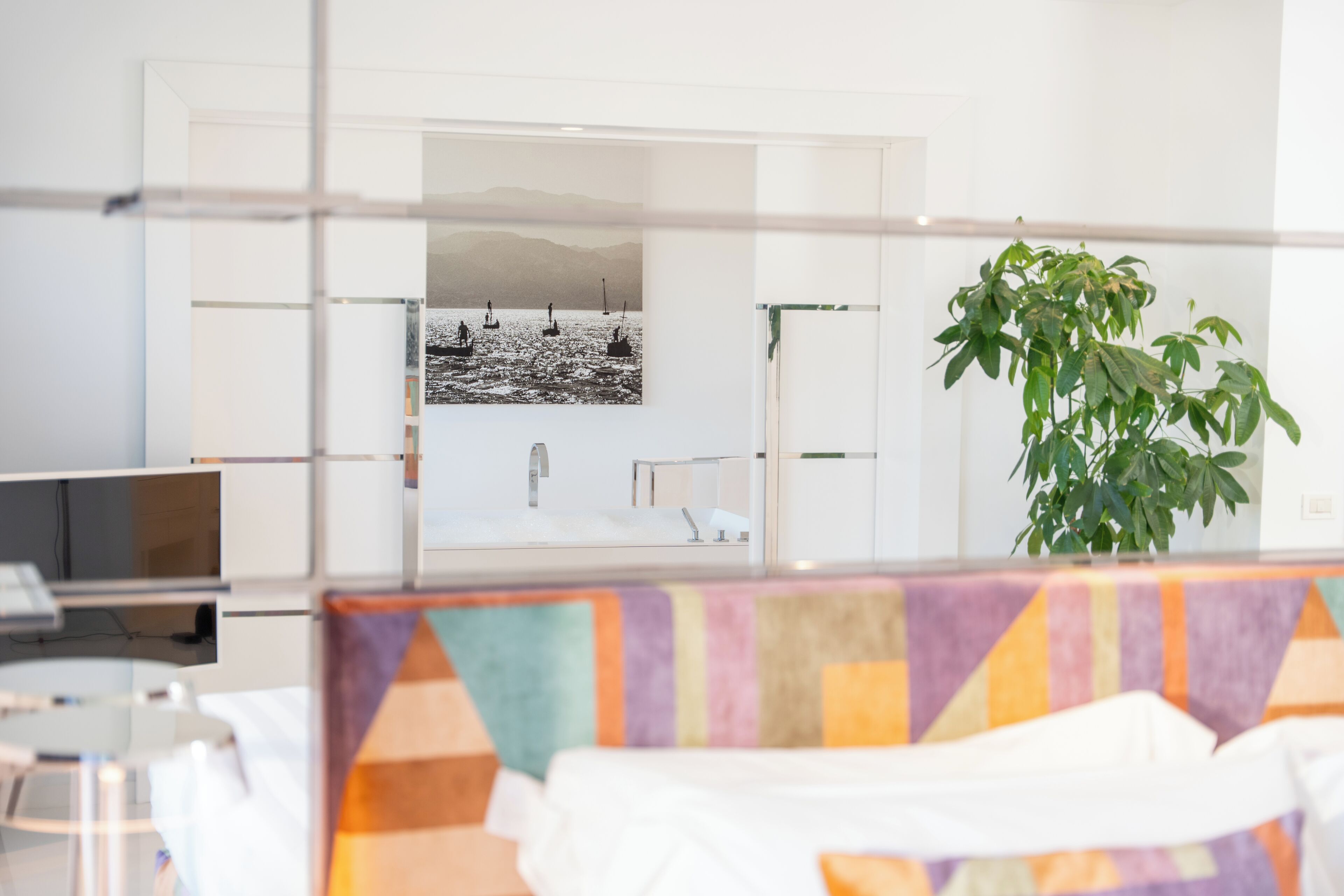 A hotel room with a bed, a television, a plant, and a view of a body of water with boats.