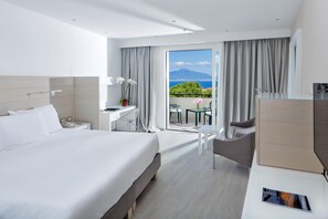 Ein modernes Hotelzimmer mit einem großen Bett, einem Schreibtisch, einem Sessel und einem Balkon mit Blick.