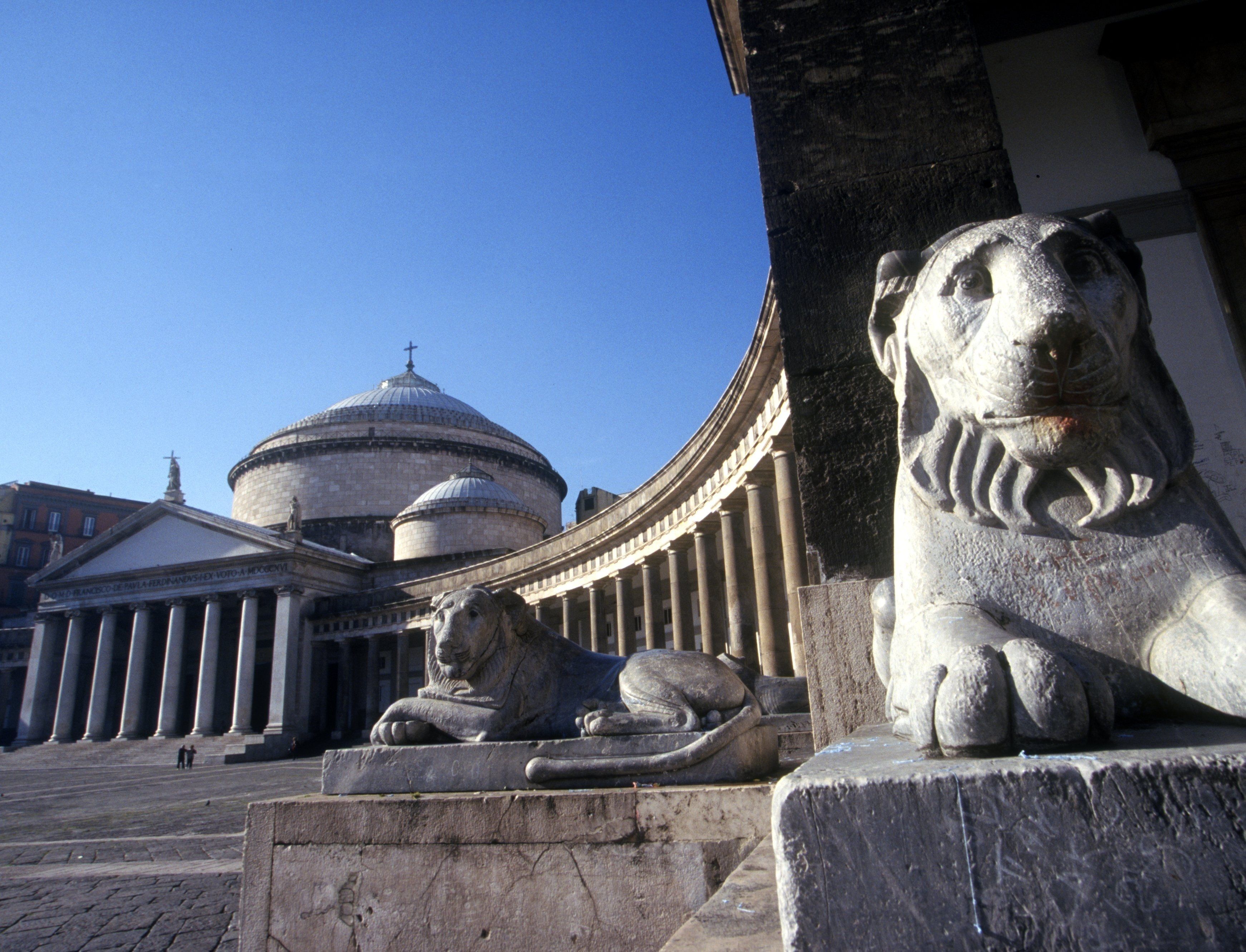 A stone lion statue and a building with classical architecture, including columns and a dome.